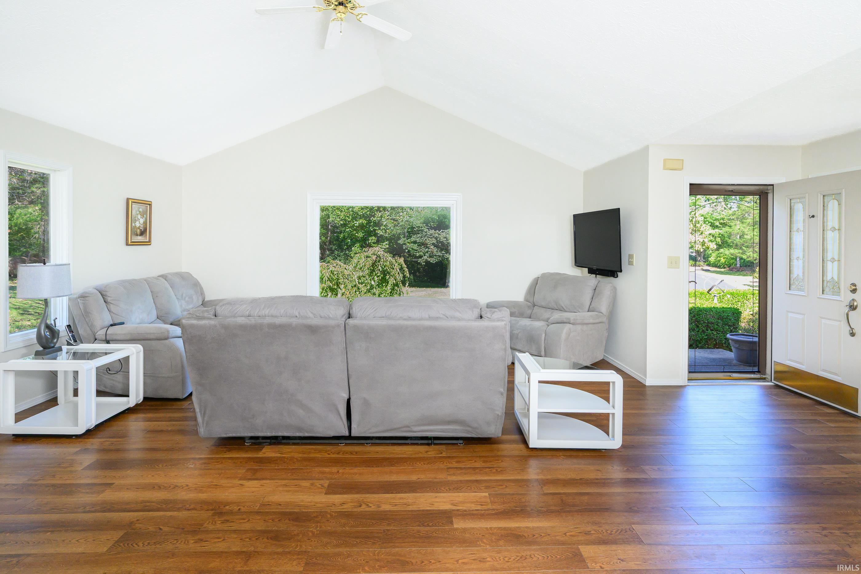 Furnished living room with vaulted ceiling, hardwood floors, gray sectional seating, and an open front door.