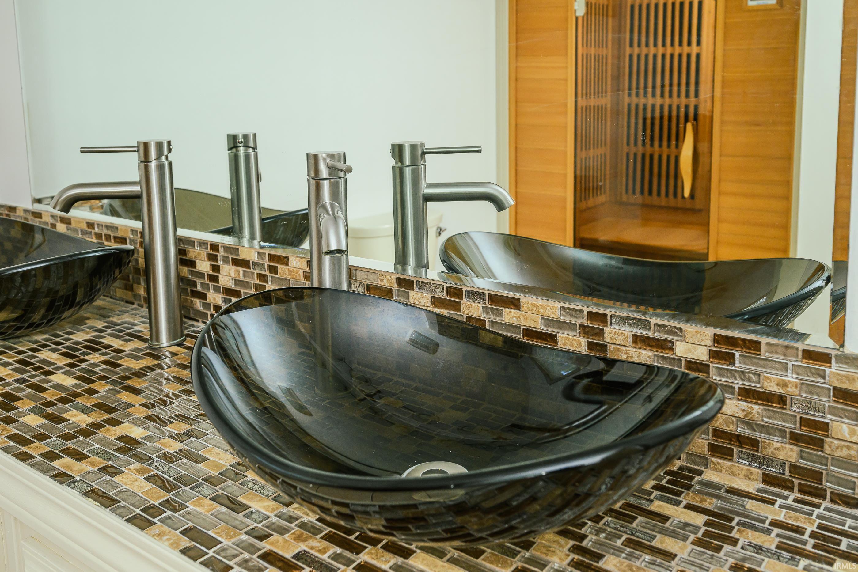 Bathroom vanity with two black glass vessel sinks, brushed-metal faucets, and brown mosaic tile.