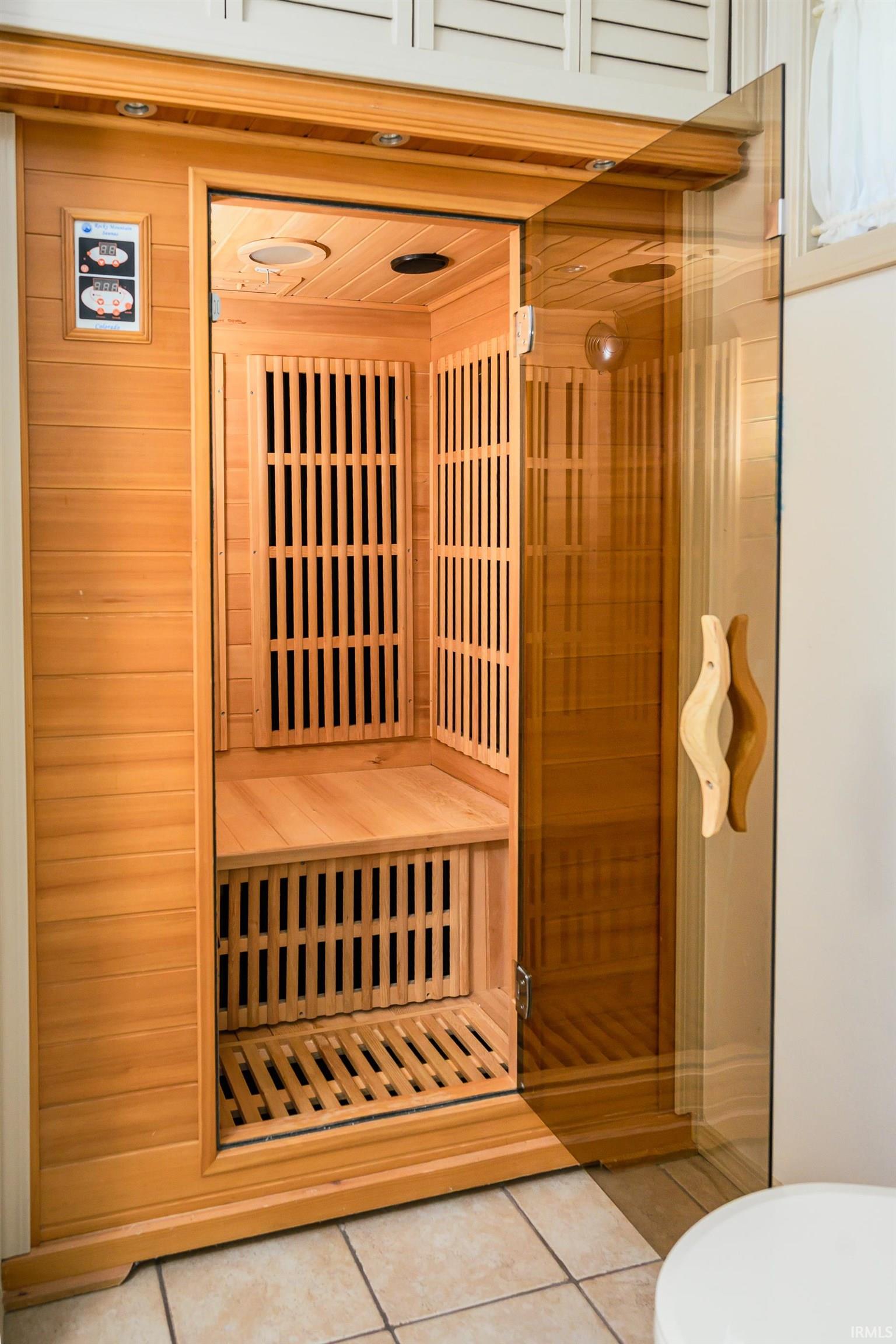 Wooden infrared sauna with slatted benches, heating panels, and an open glass door.