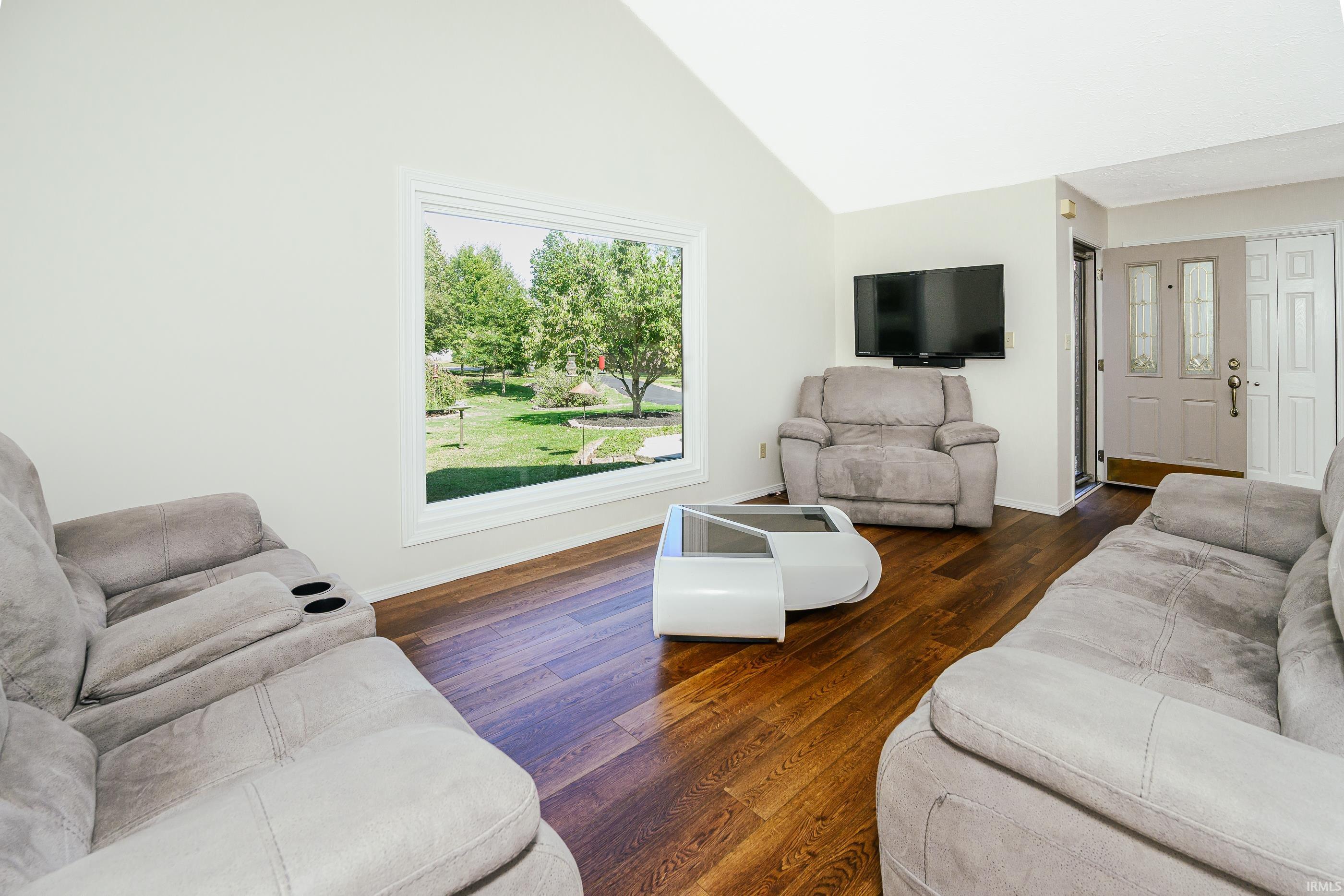 Living room with gray recliners, dark hardwood floors, and a large window overlooking a leafy yard.