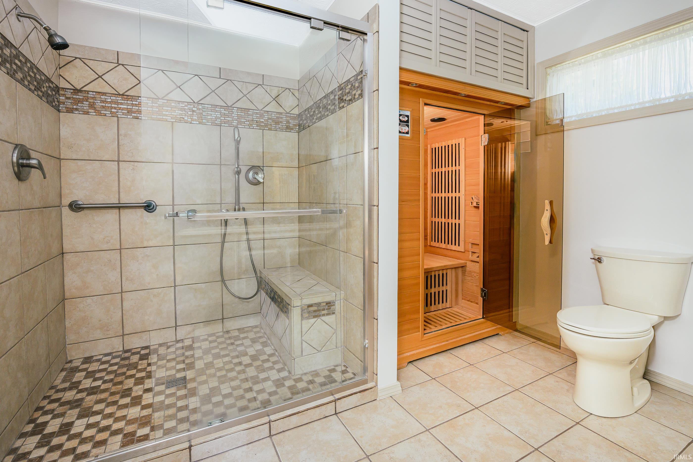 Bathroom with a tiled walk-in shower, built-in bench, wooden sauna, and toilet.