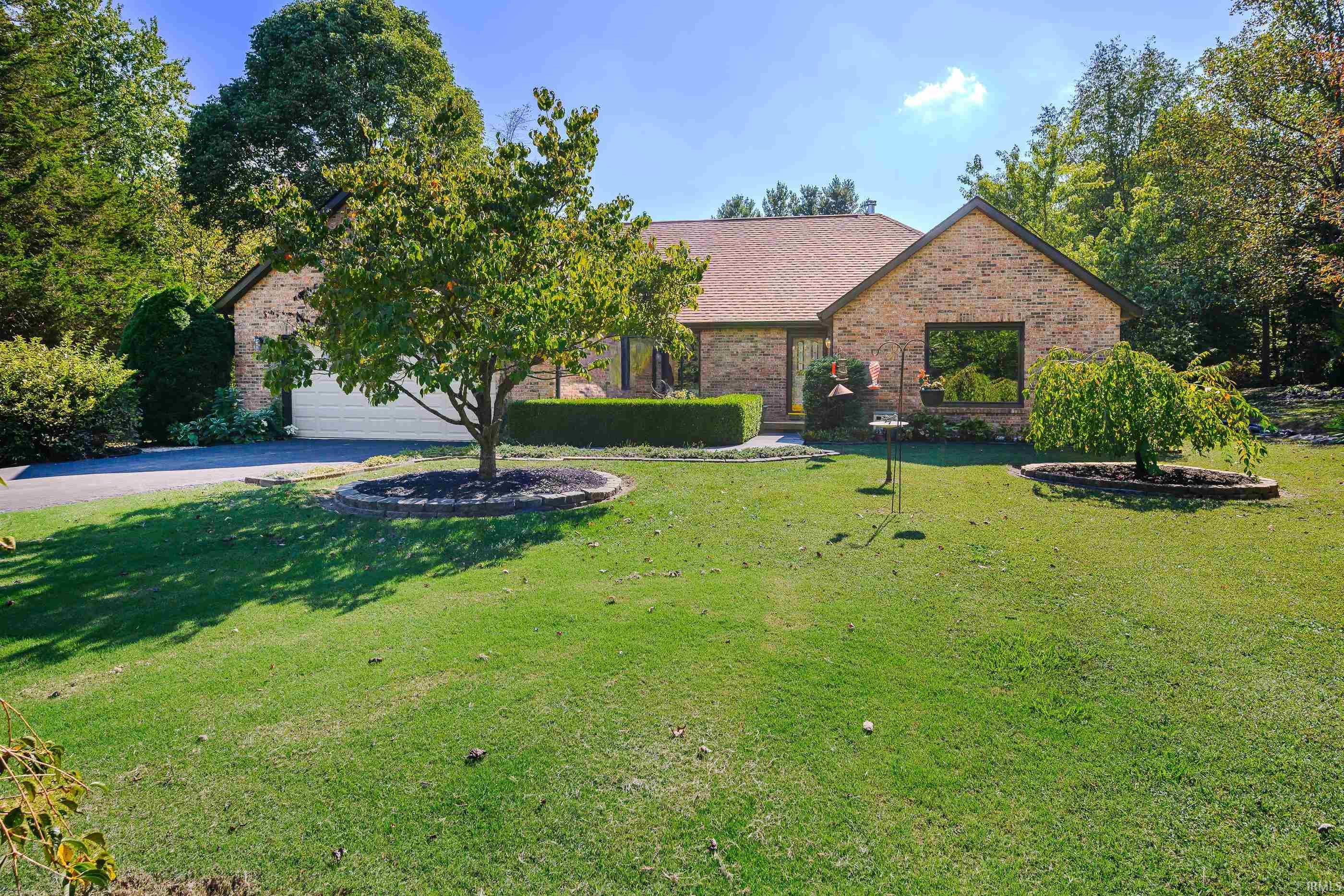 Brick house with an attached garage, framed by mature trees and a broad green lawn.