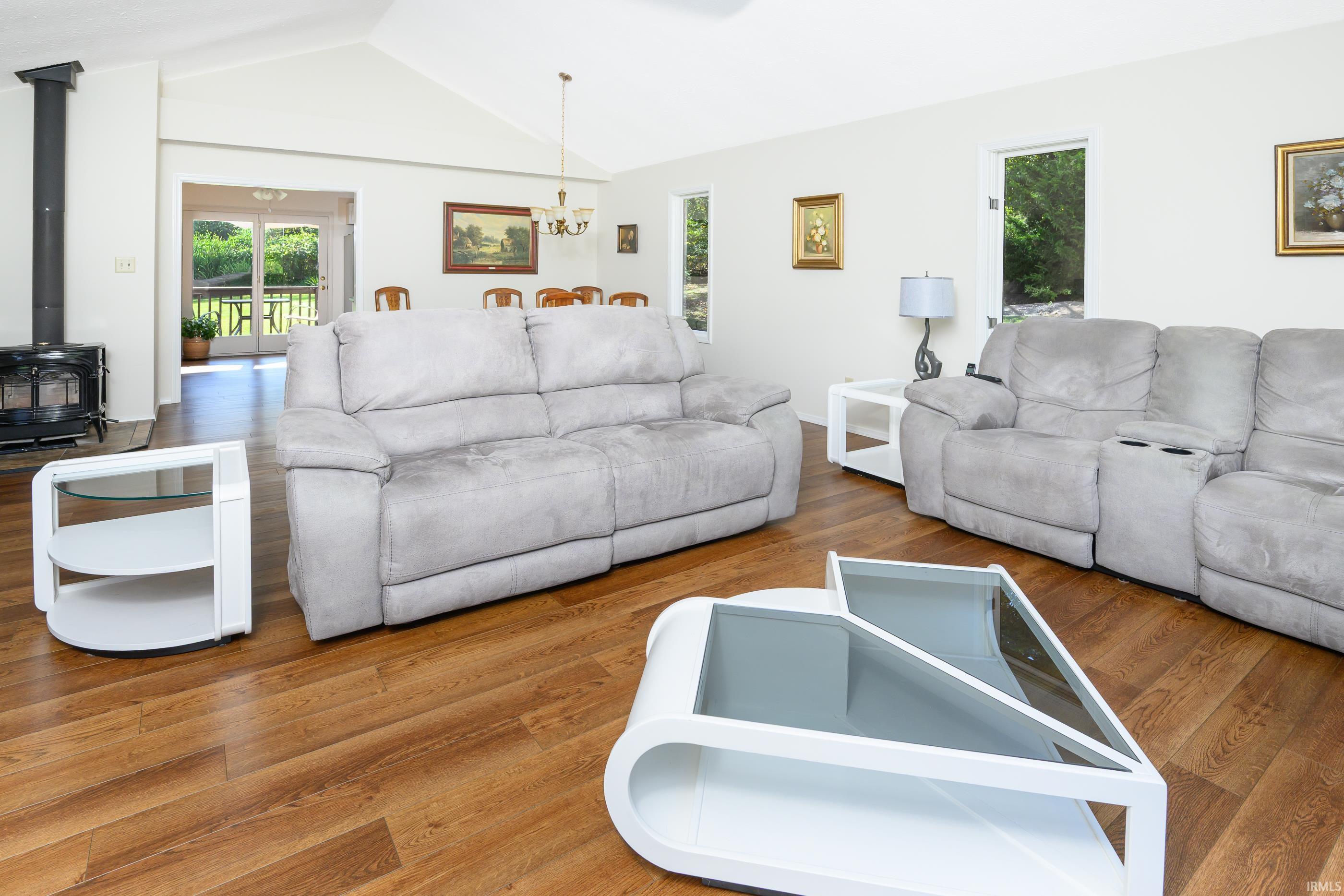 Living room with light-gray sofas, a black wood stove, and glass doors opening to greenery.