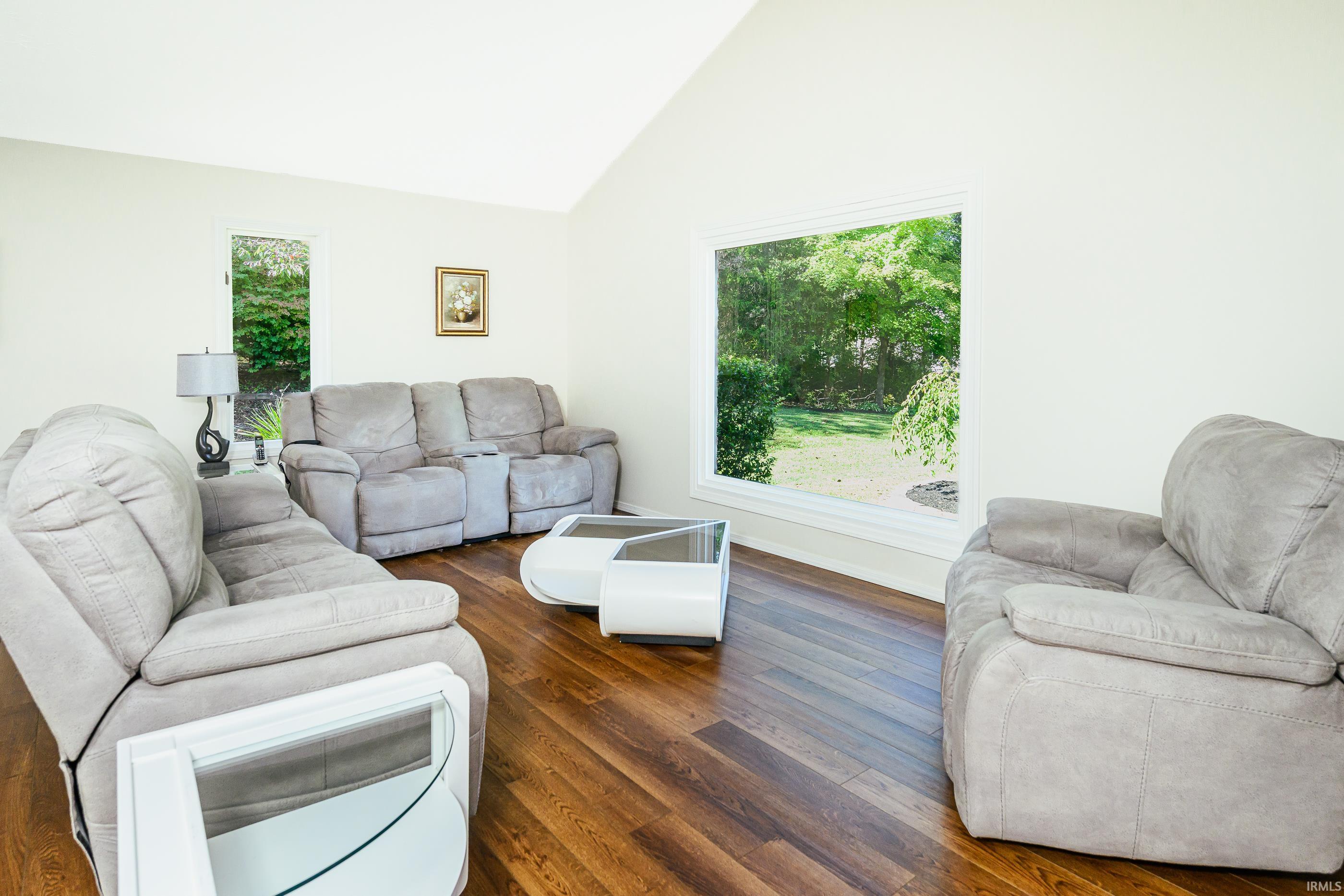 Living room with gray recliners, dark wood floors, and a large window overlooking a leafy yard.