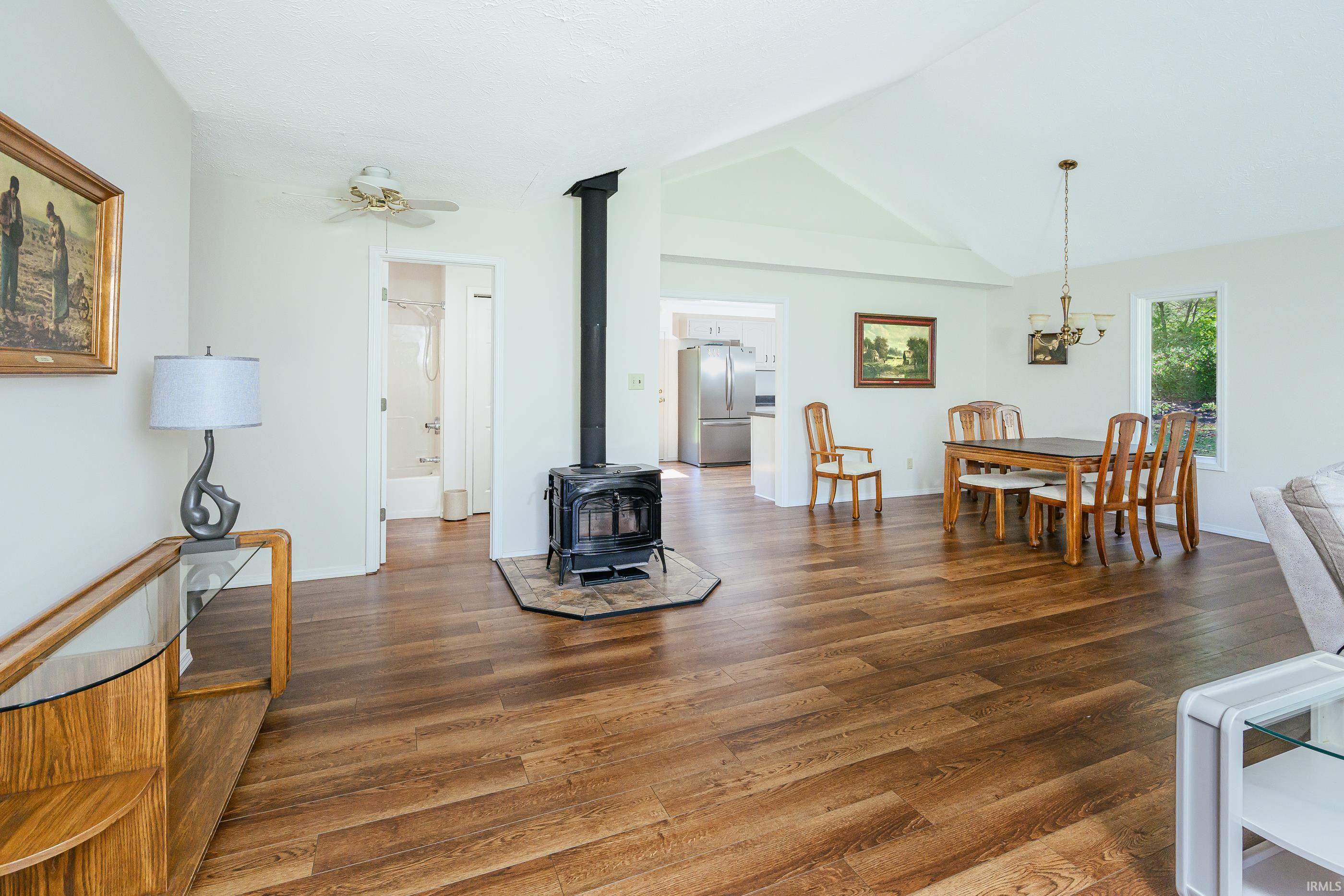 Open-plan living and dining room with hardwood floors, vaulted ceiling, and freestanding wood stove.