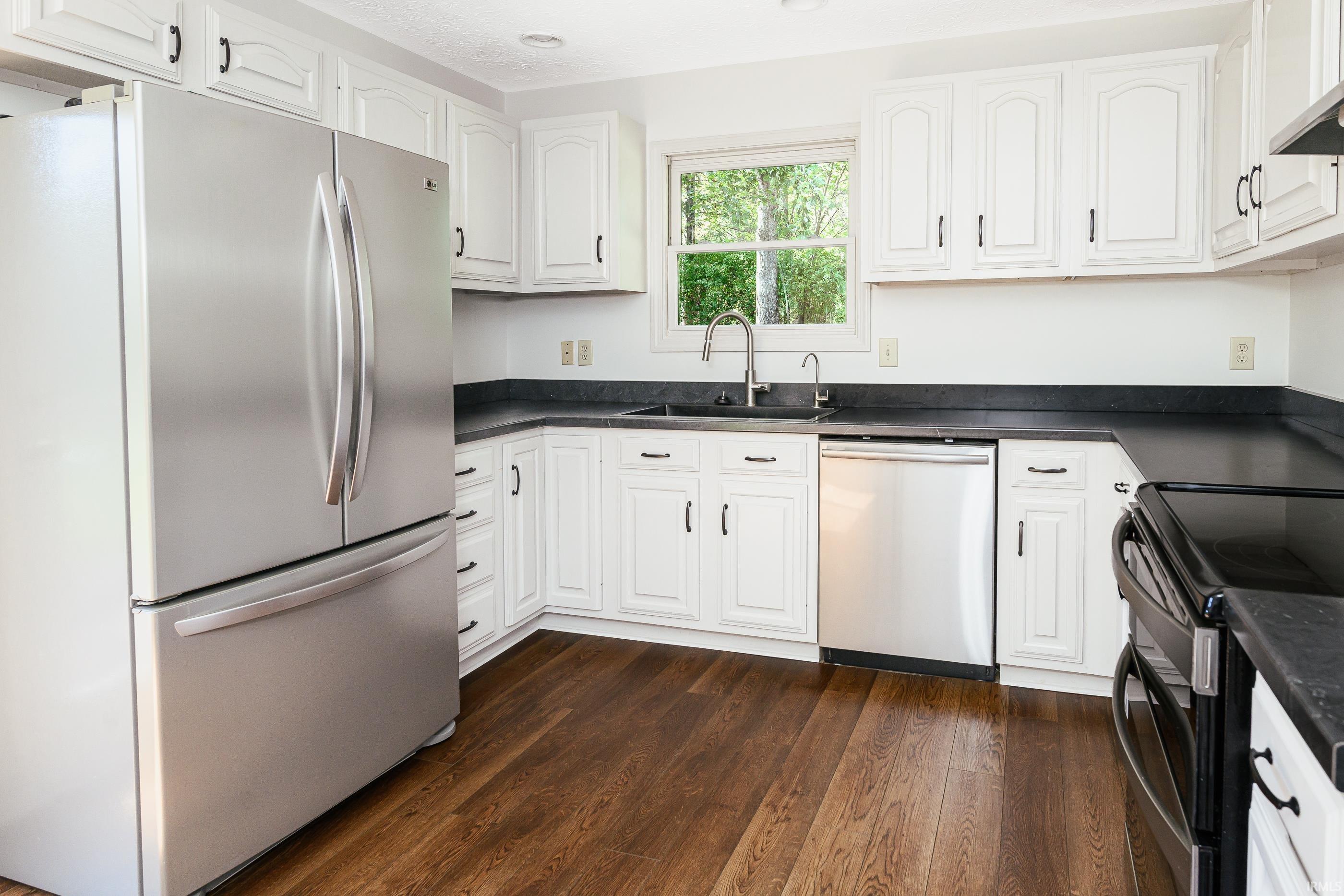 Kitchen with white cabinets, dark countertops, stainless steel appliances, and dark wood flooring.
