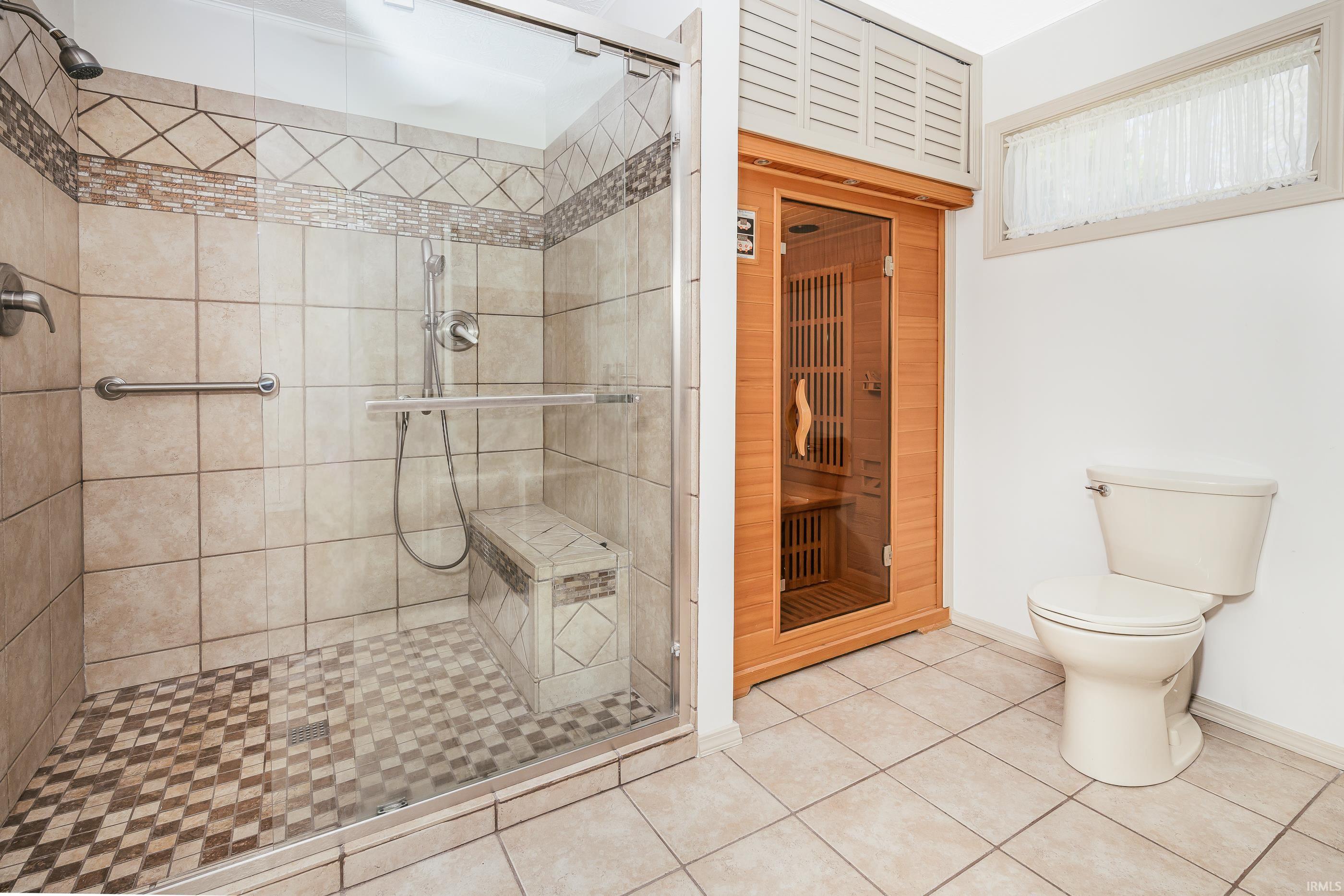 Bathroom with a tiled walk-in shower, built-in bench, and wood-paneled sauna.