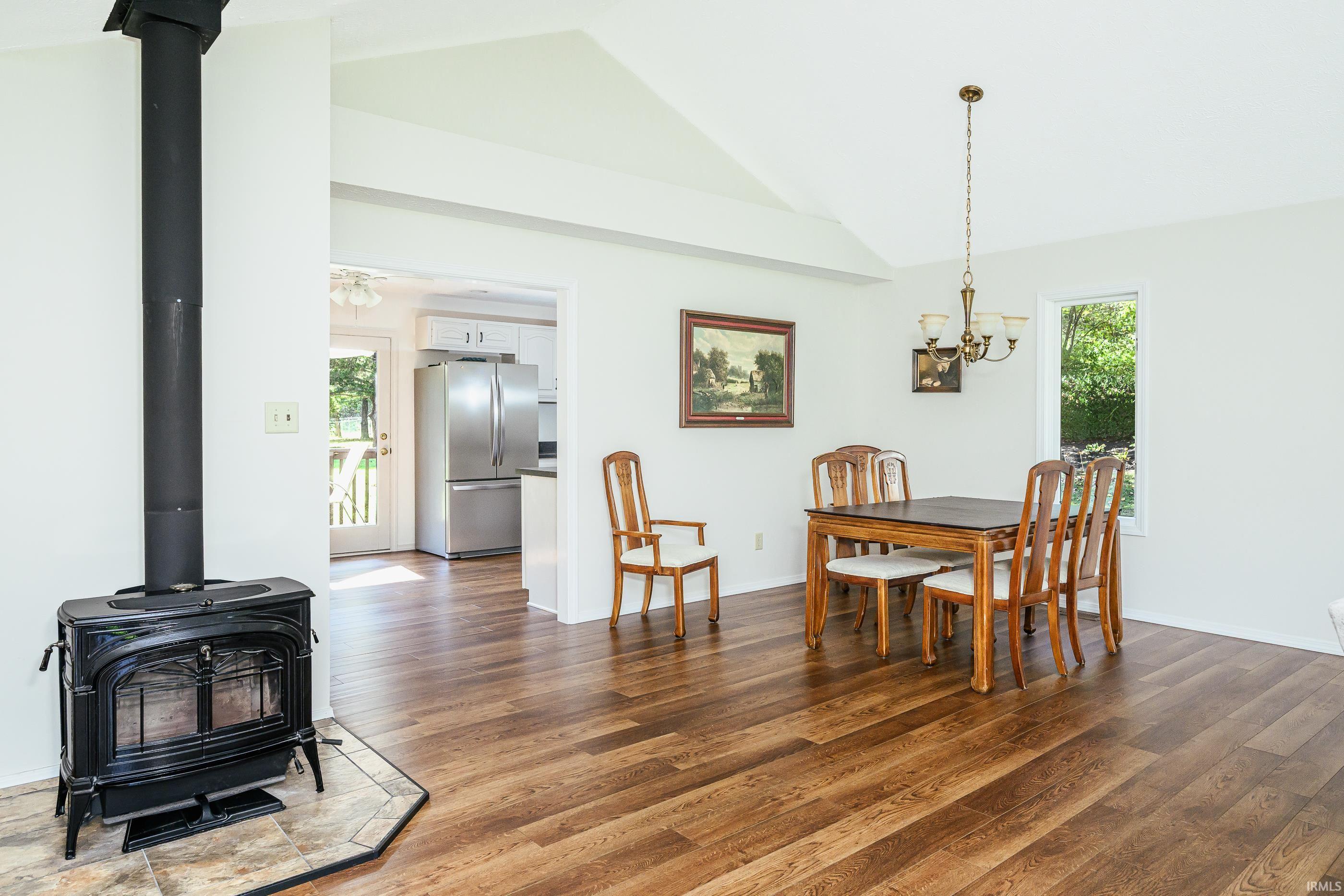 Dining area with a wooden table and chairs, hardwood floors, and a black wood stove on a tiled hearth.