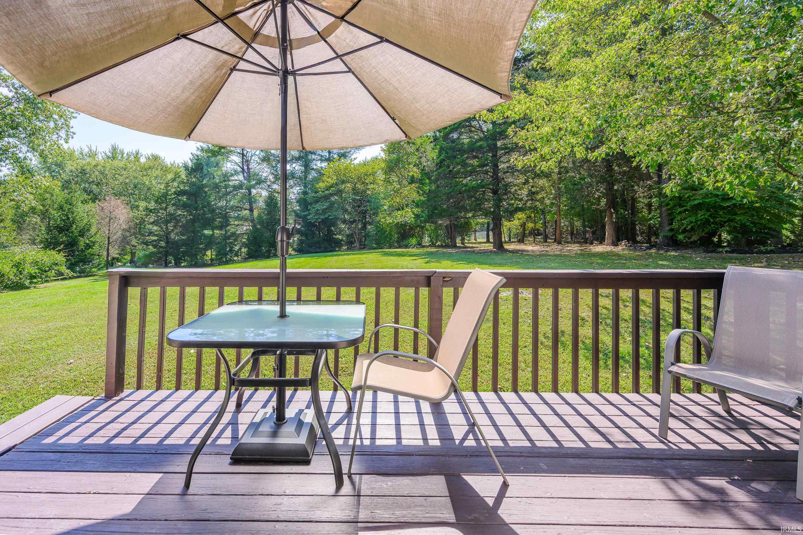 Deck with umbrella-shaded patio table and chairs overlooking a tree-lined lawn.