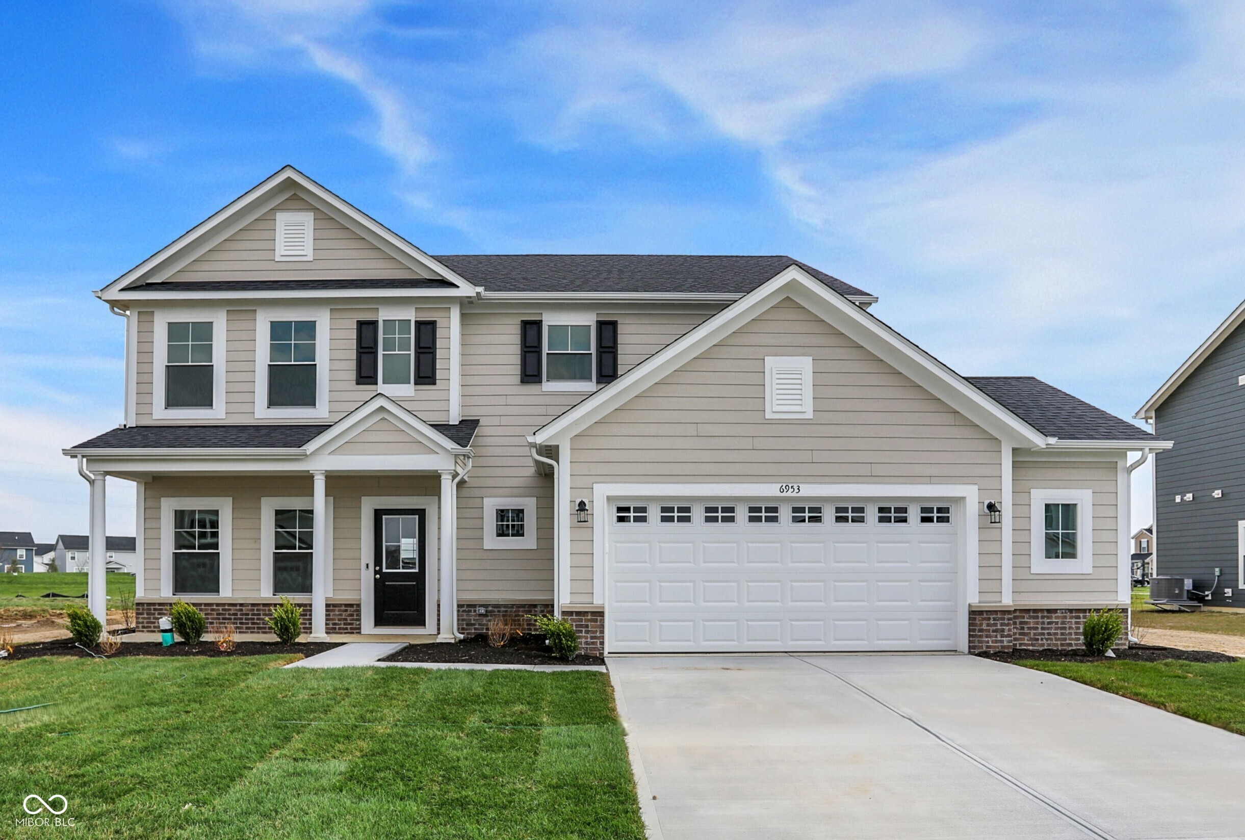 Two-story beige house with a covered porch, white trim, and attached two-car garage.