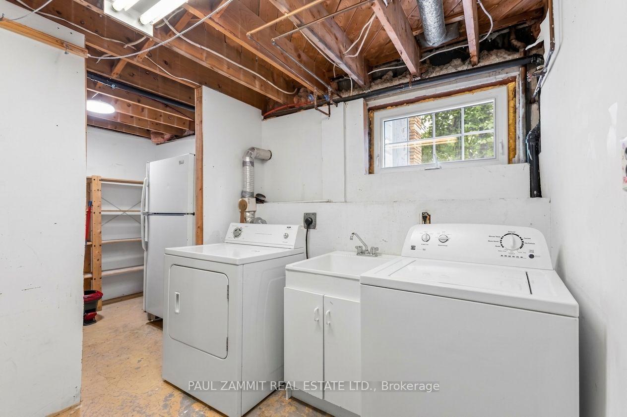 Laundry room with white washer and dryer, utility sink, exposed ceiling joists, and a small window.