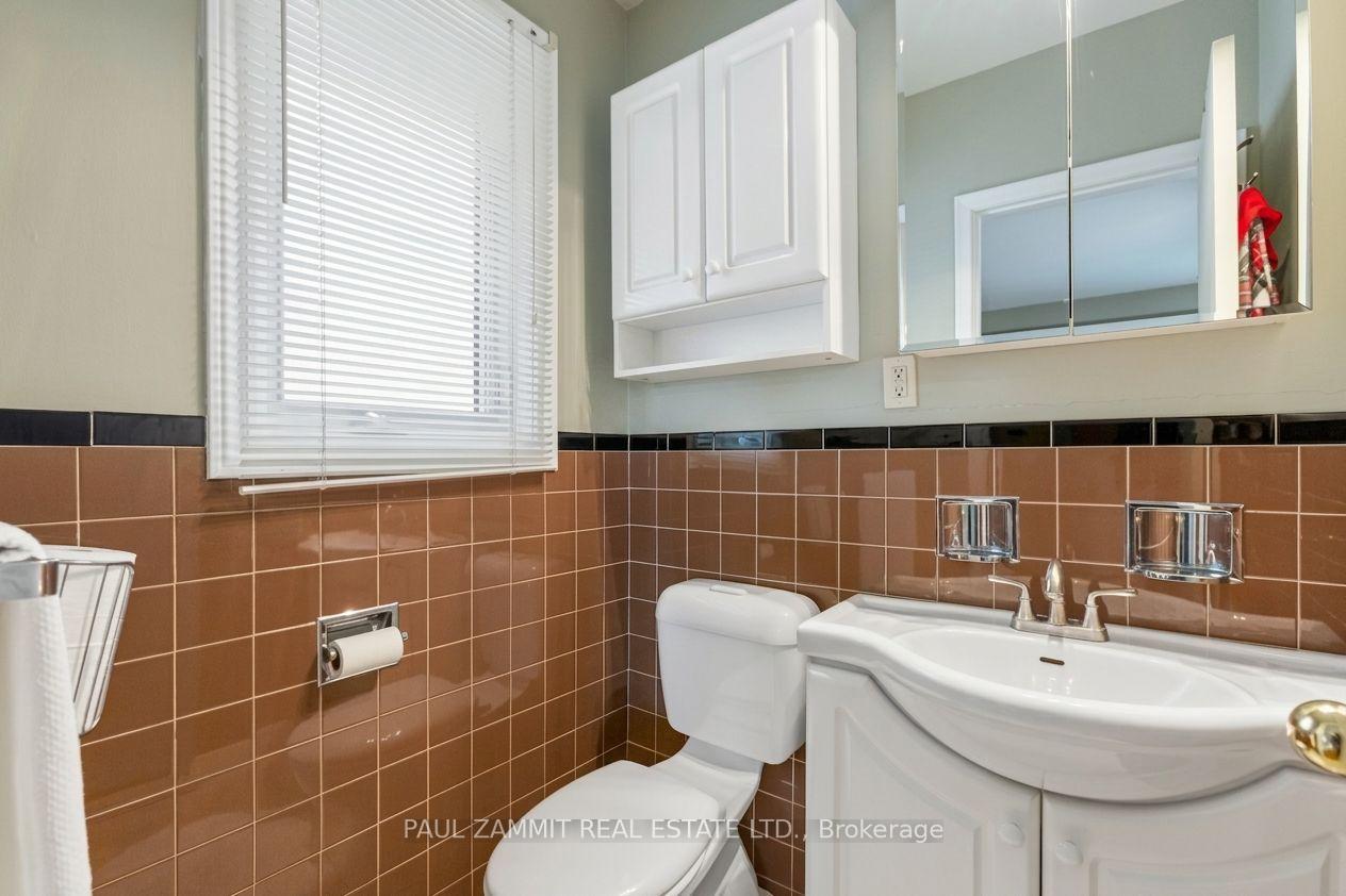 Bathroom with brown tile walls, white toilet and sink vanity, and a window with blinds.