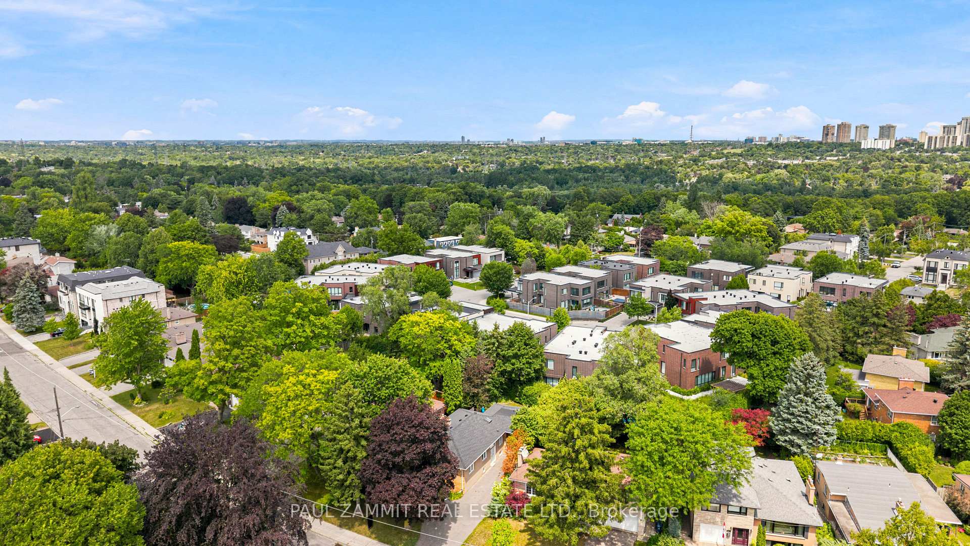 Aerial view of a leafy Toronto neighborhood with modern homes and distant high-rises.