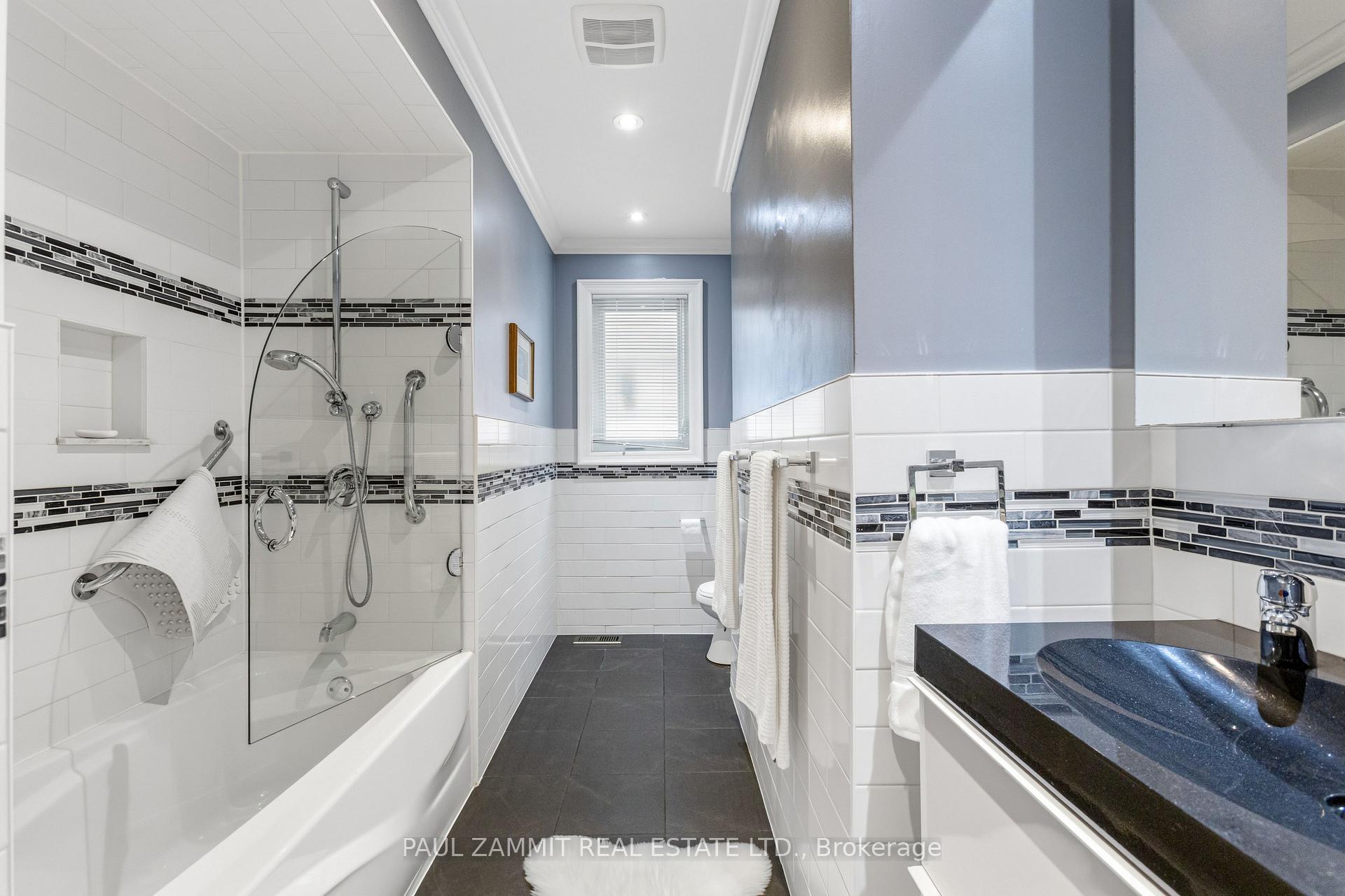 Bathroom with a glass-enclosed tub-shower, dark mosaic tile accents, and a dark vanity.