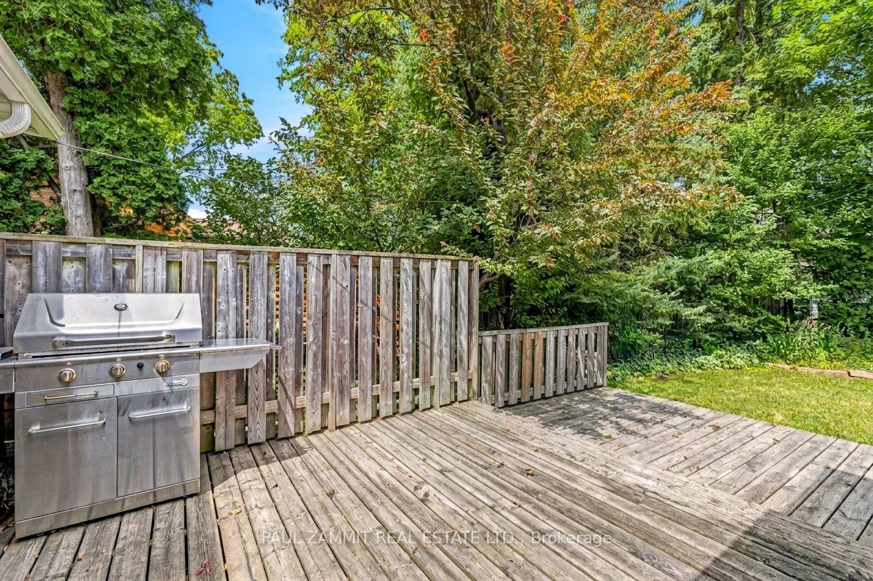 Backyard deck with a stainless steel gas grill, wooden privacy fence, and leafy trees.