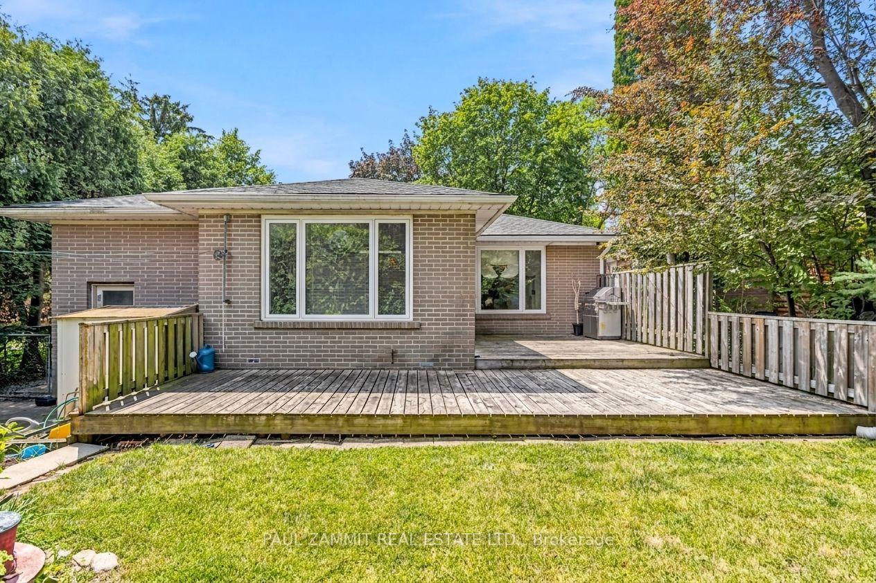 Brick home’s rear exterior with a broad wooden deck, fenced patio, and leafy backyard.