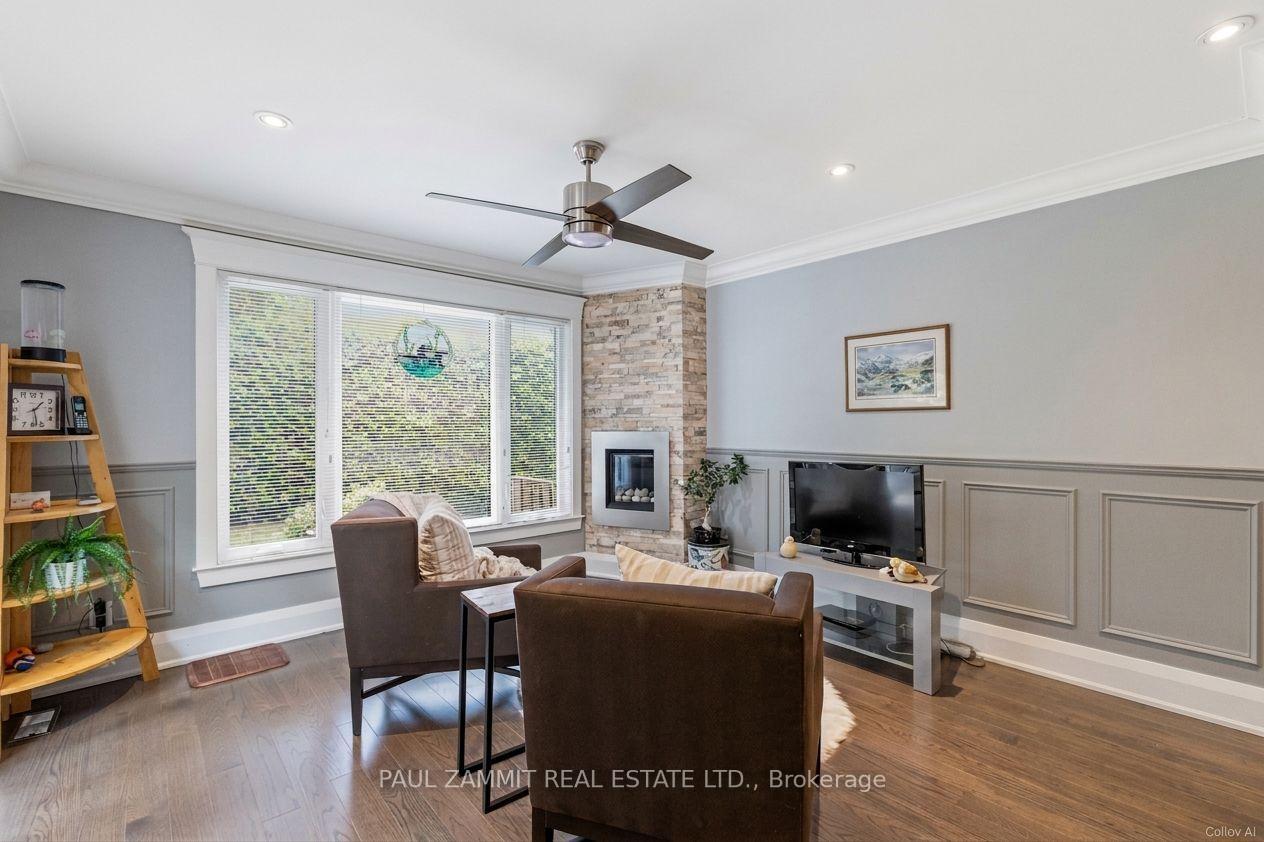 Furnished living room with a stone fireplace, large windows, and a ceiling fan.