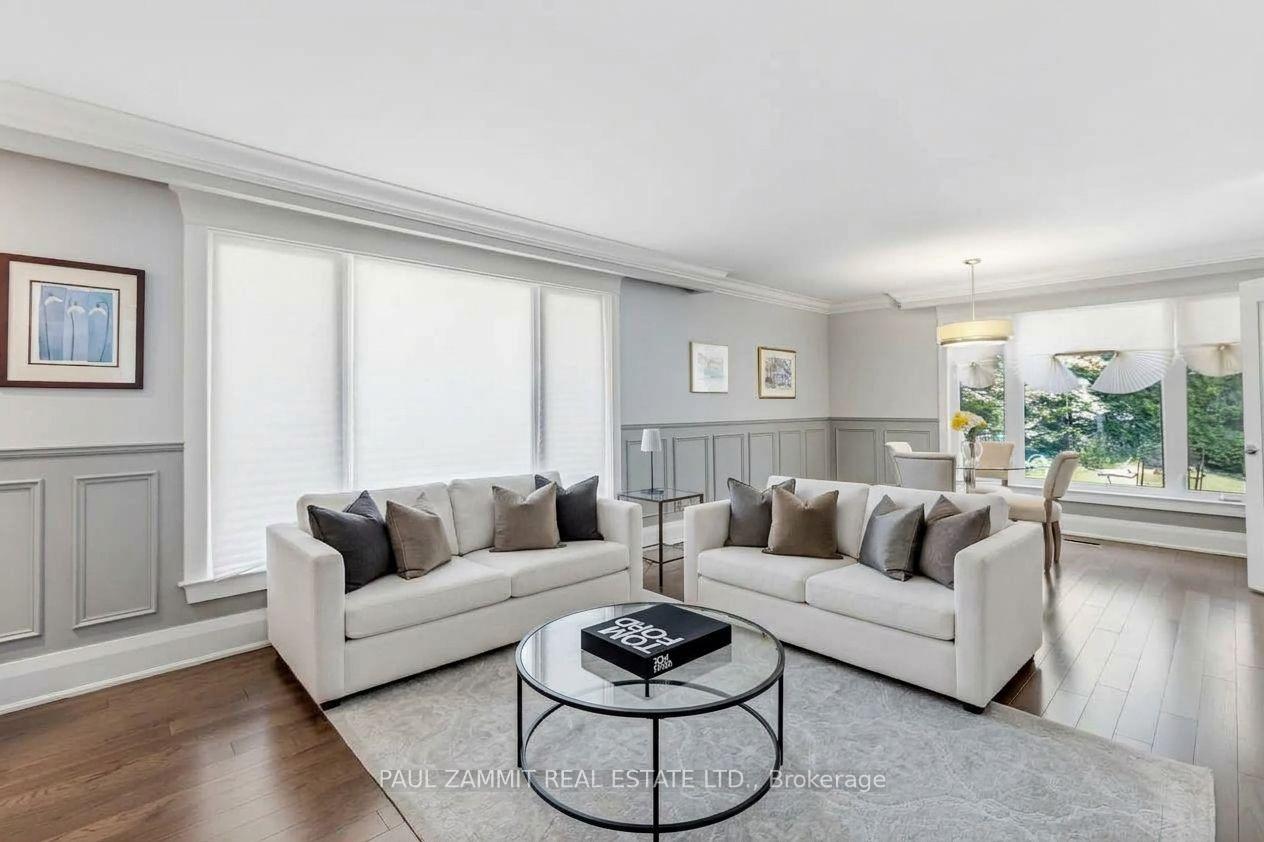 Staged living room with two white sofas, a round glass coffee table, and large windows overlooking greenery.