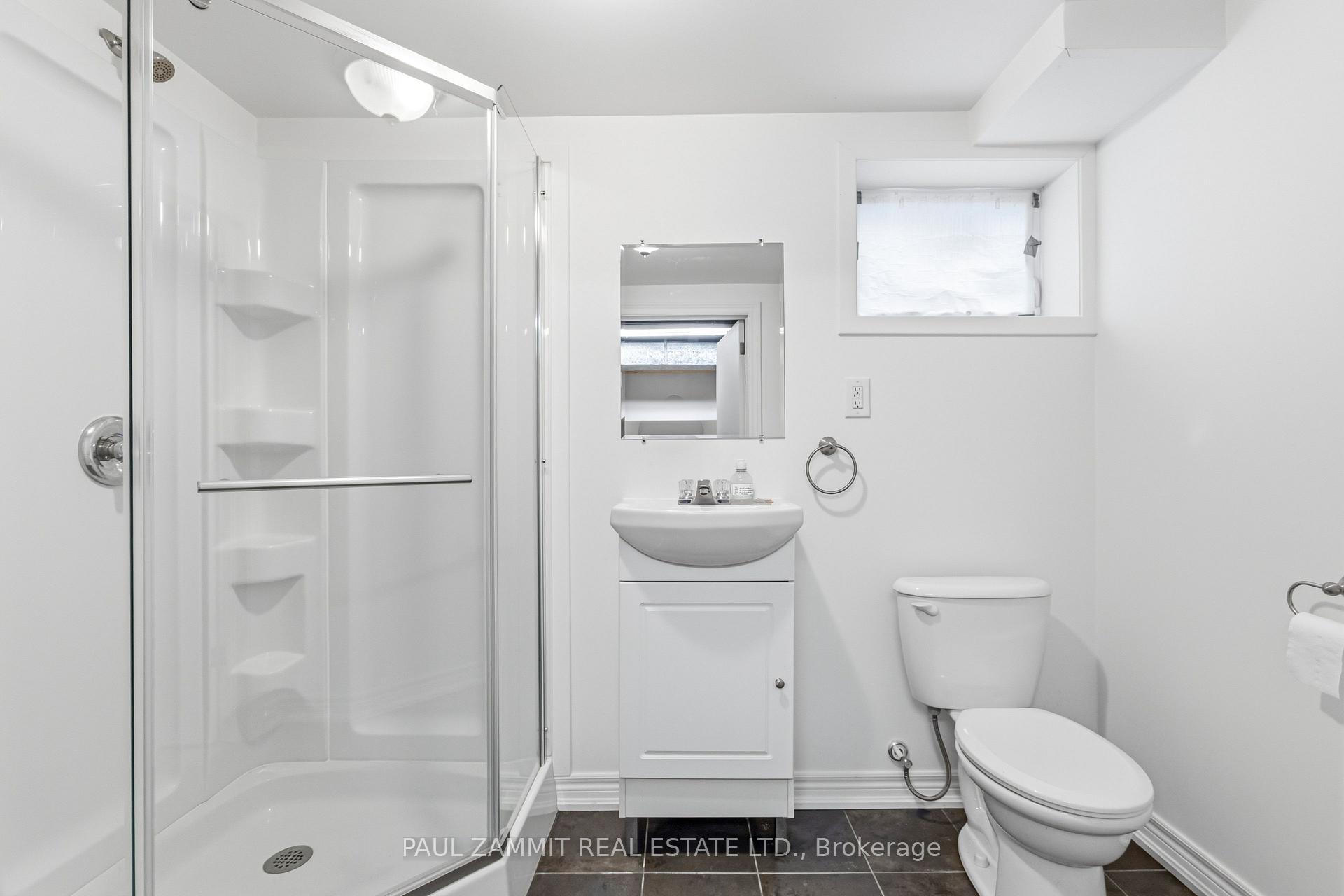 White bathroom with glass shower, corner shelves, vanity sink, and toilet.