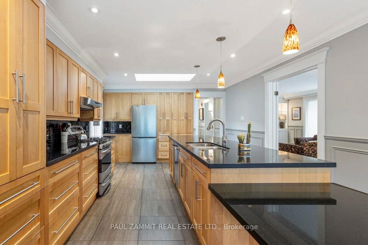 Kitchen with honey-toned cabinets, black countertops, stainless steel appliances, and a large island.