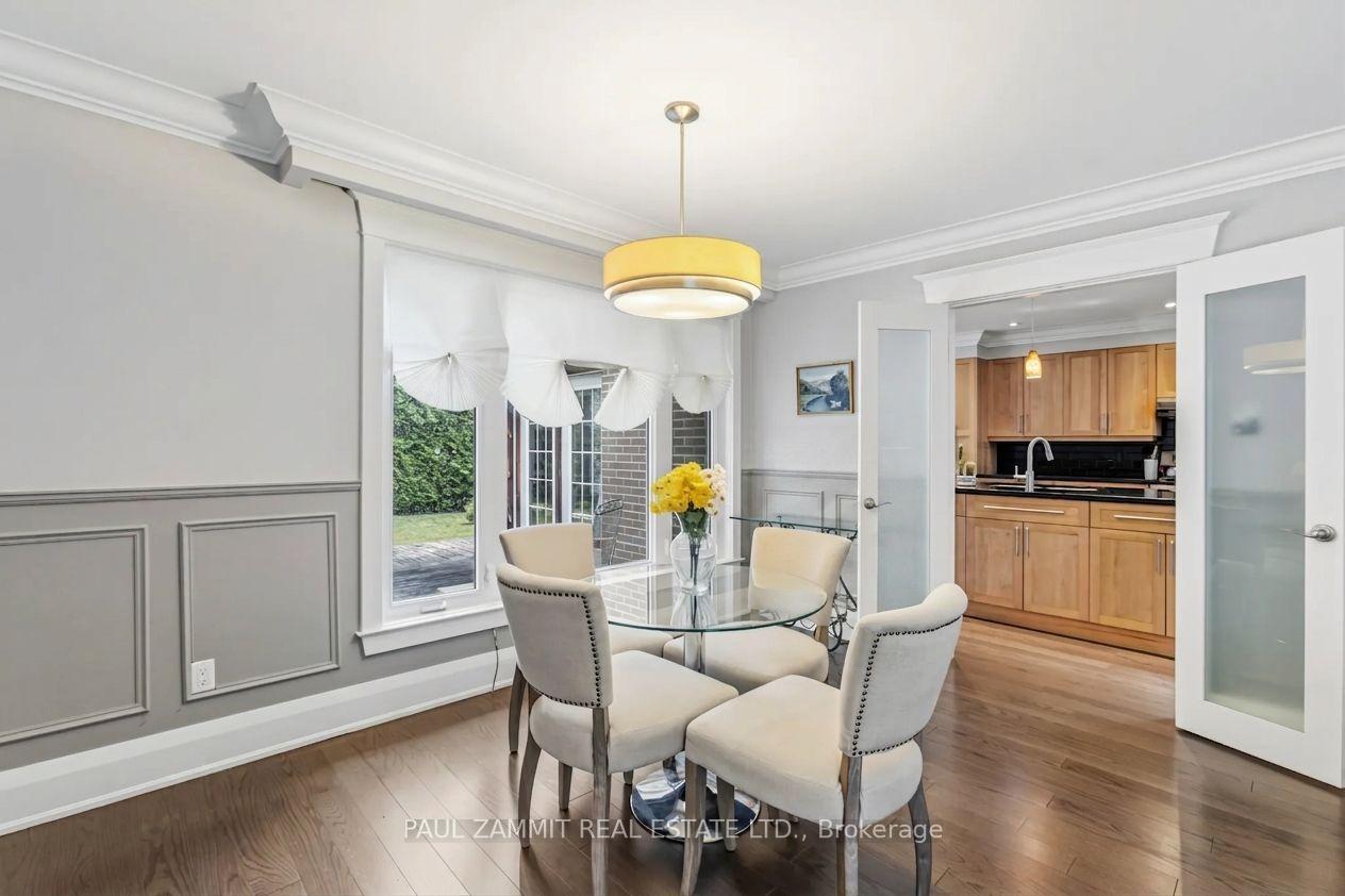 Dining room with a glass table, cream chairs, paneled walls, and an open view into the kitchen.