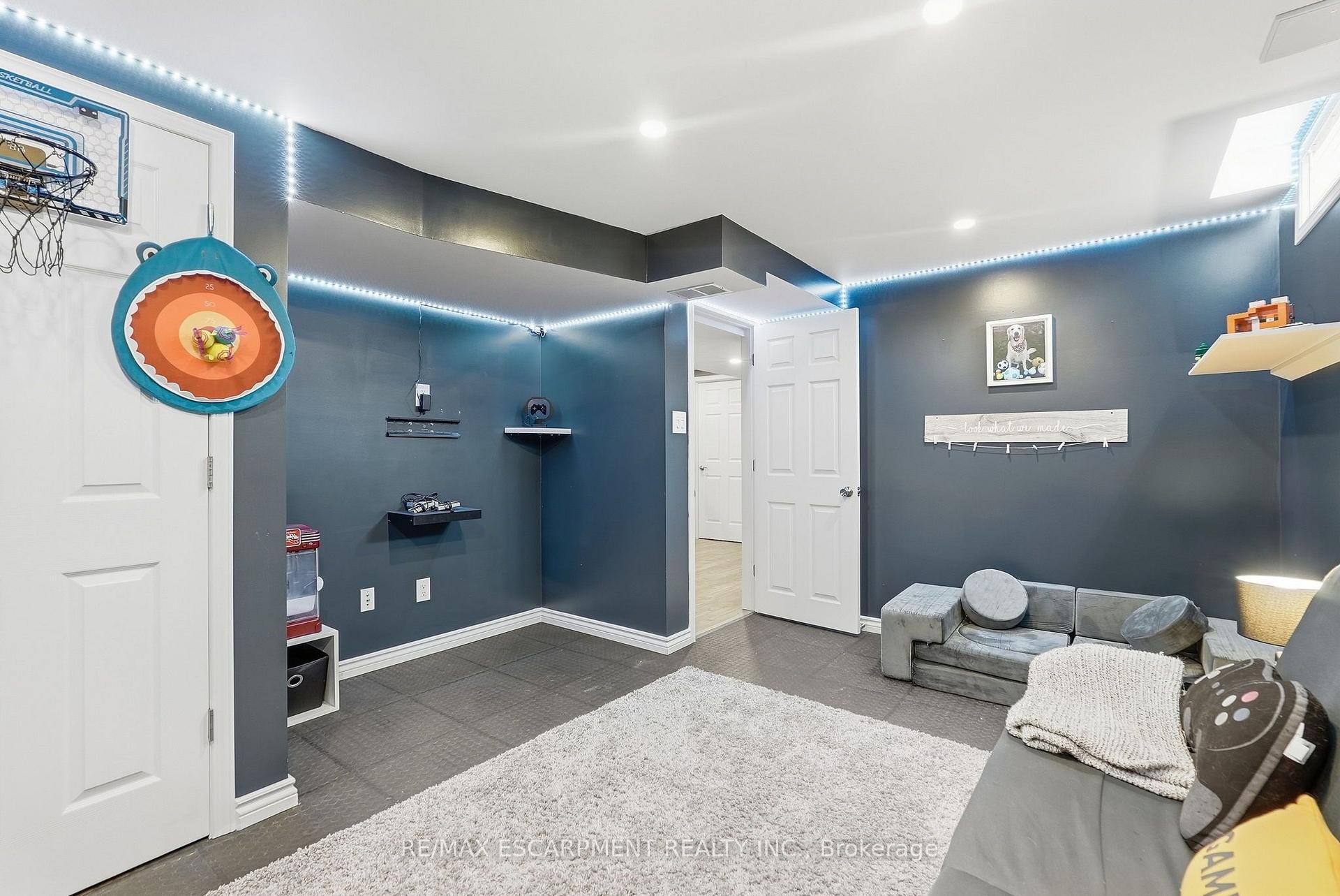 Basement recreation room with a gray sectional, gaming equipment, basketball hoop, and colorful wall target.