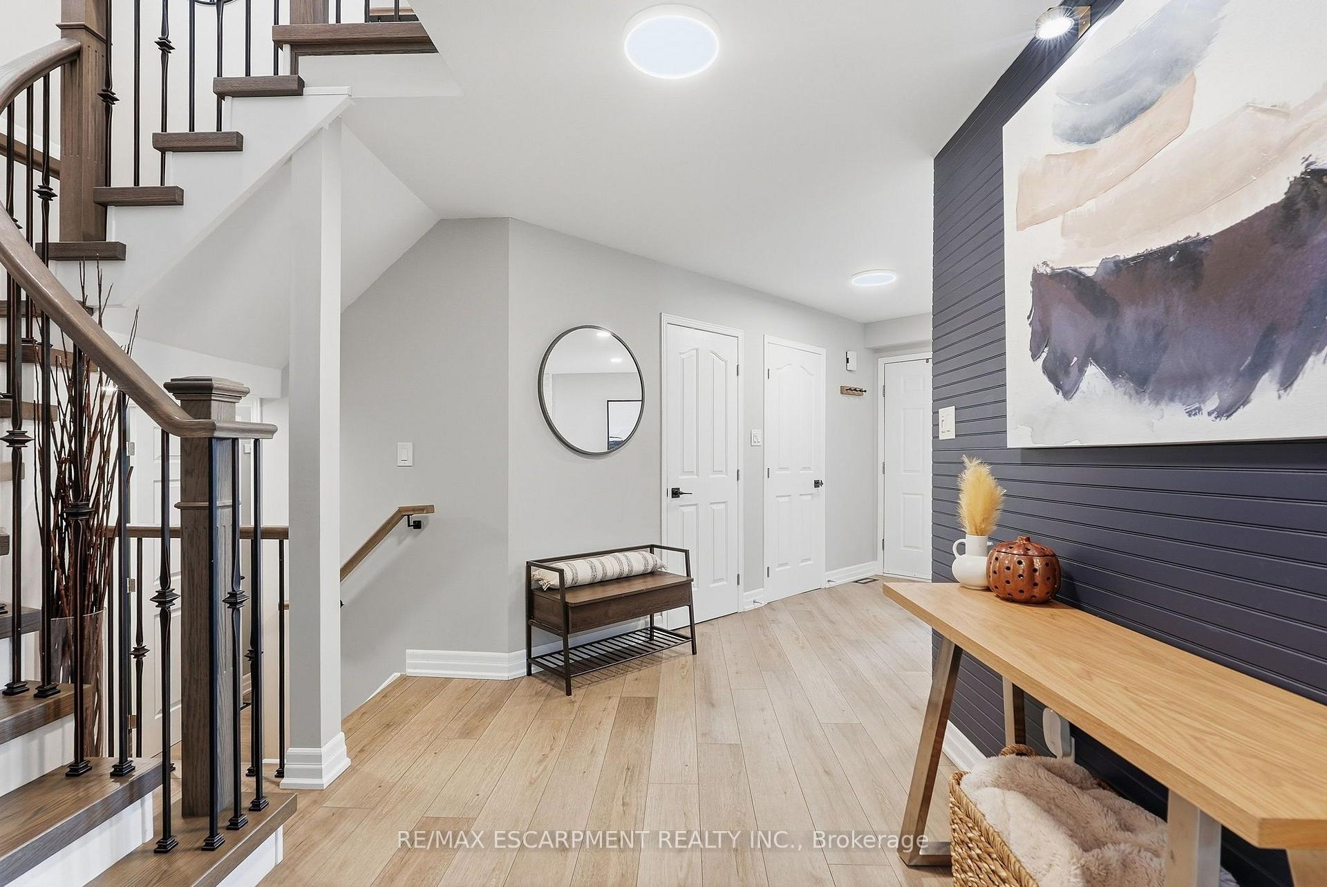 Home foyer with a dark wood staircase, round mirror, and dark accent wall with abstract artwork.