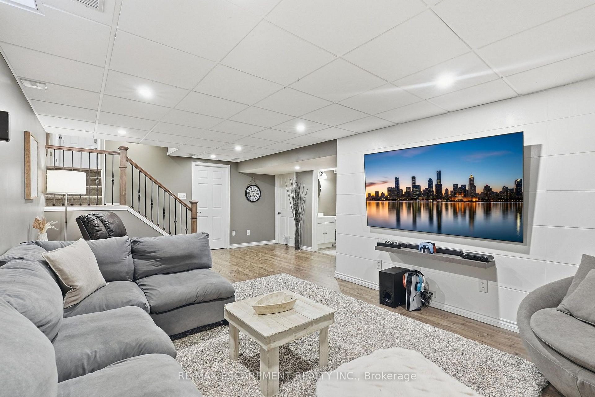 Basement family room with a gray sectional, wall-mounted television, and staircase.