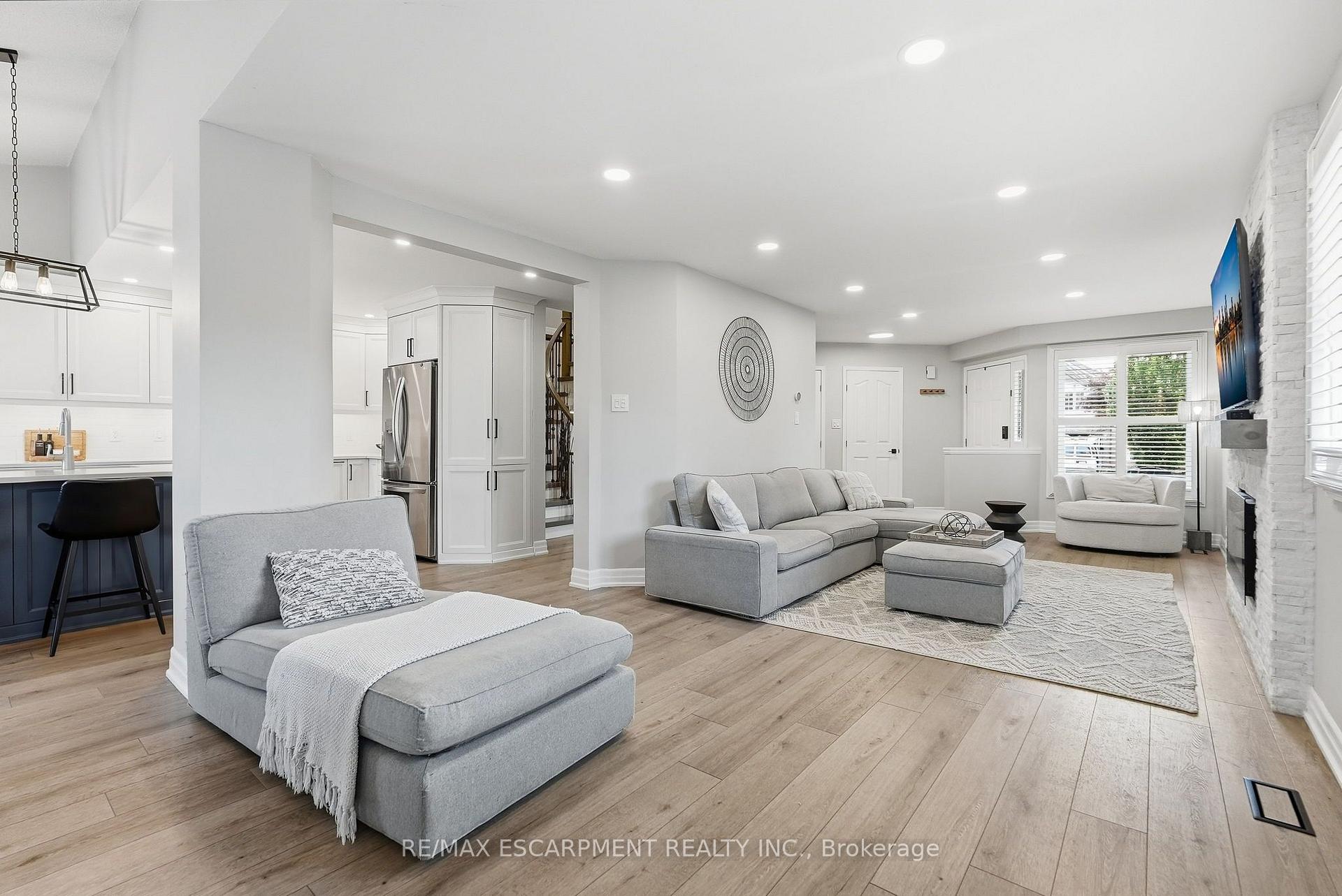 Open-concept living room with gray sectional seating, wood floors, and a white brick fireplace.