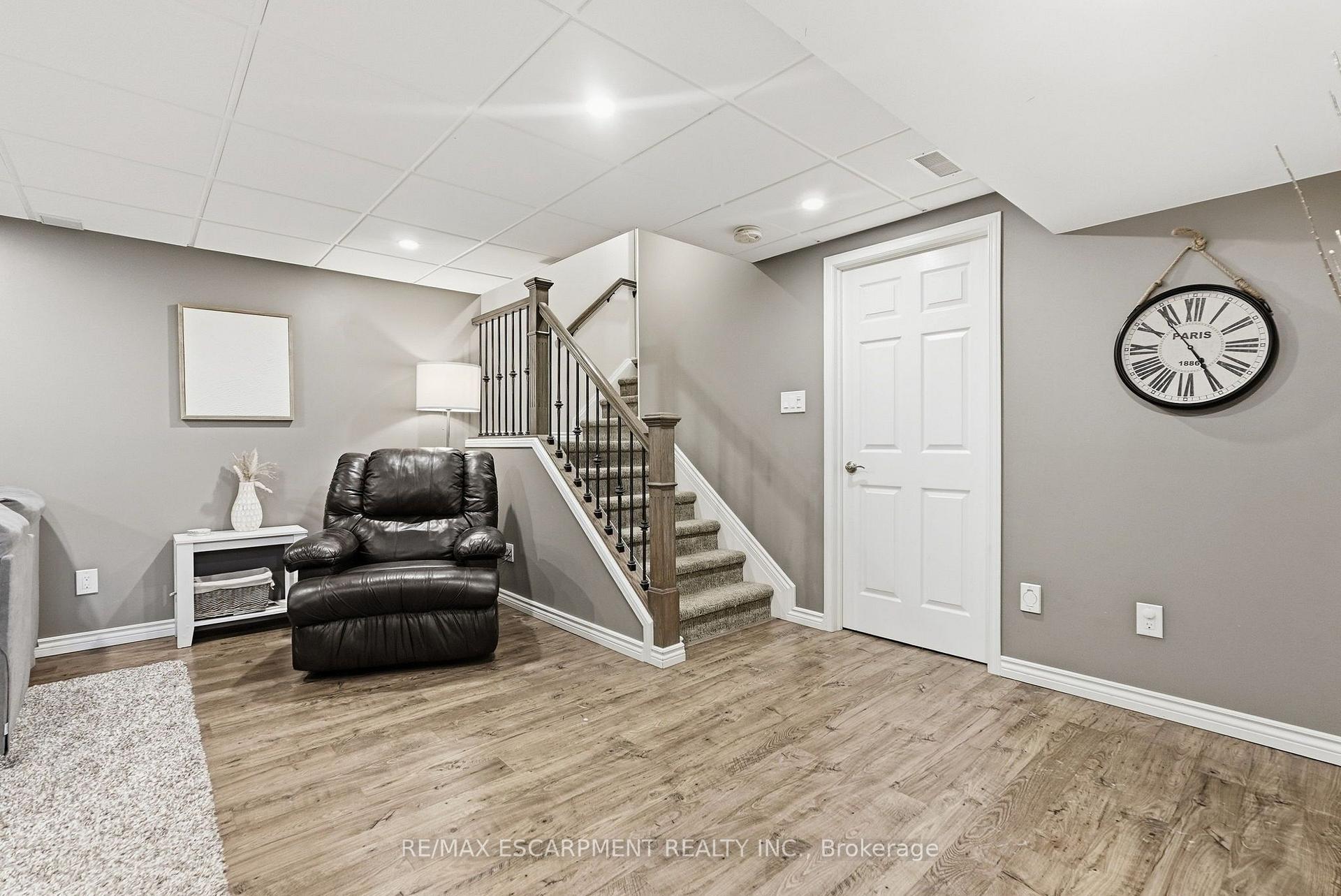 Basement sitting area with a black leather recliner beside carpeted stairs with dark railings.