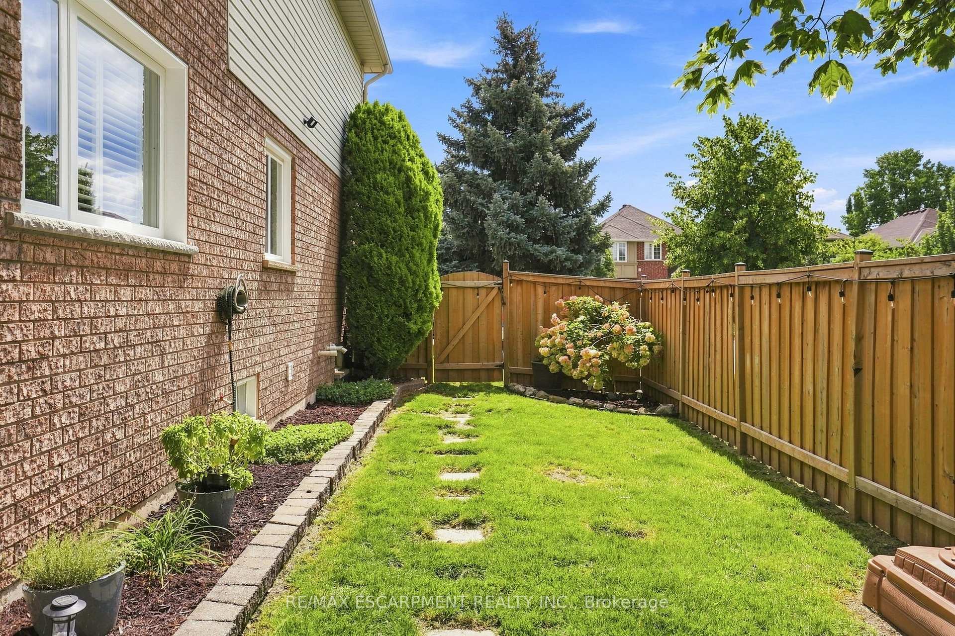 Fenced backyard with a lawn, stepping-stone path, garden beds, and string lights along the wooden fence.