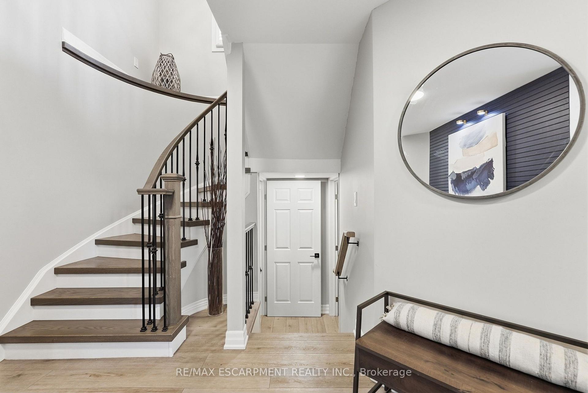 Staged foyer with a curved wood-and-metal staircase, oval mirror, and cushioned entry bench.
