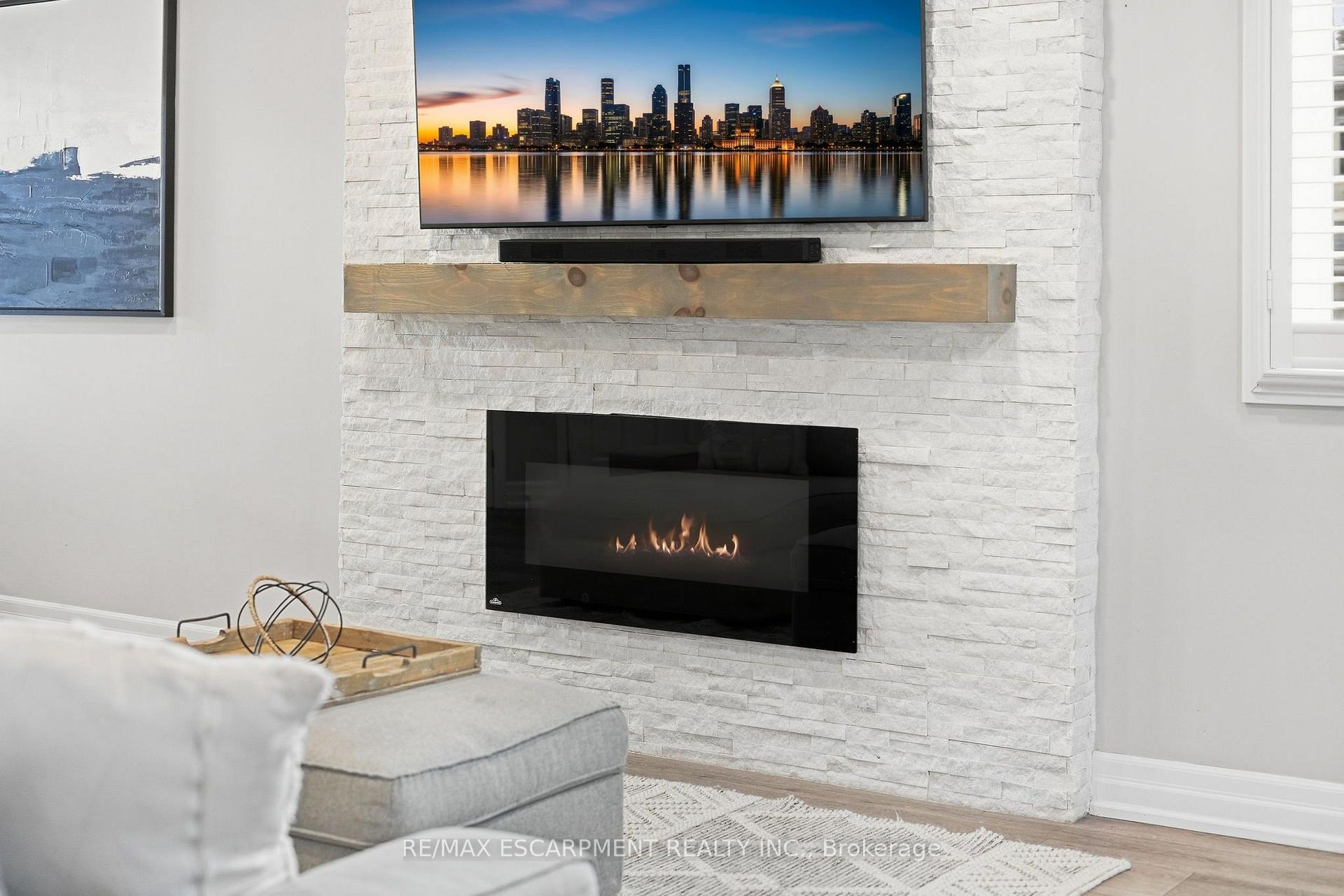 Living room with a white stone fireplace, lit linear fire, wood mantel, and television above.