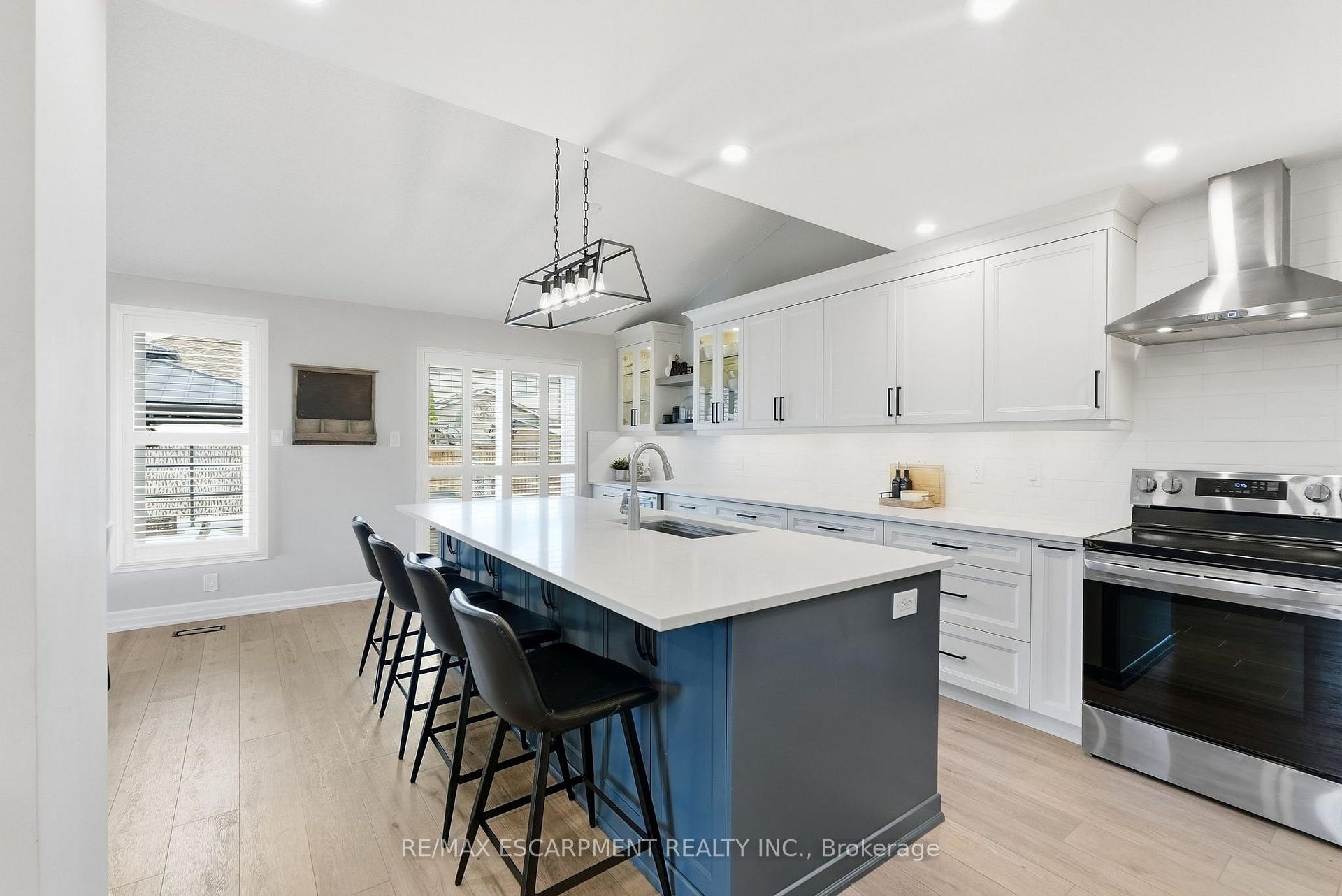 Bright white kitchen with a large blue island, bar stools, and stainless steel range.