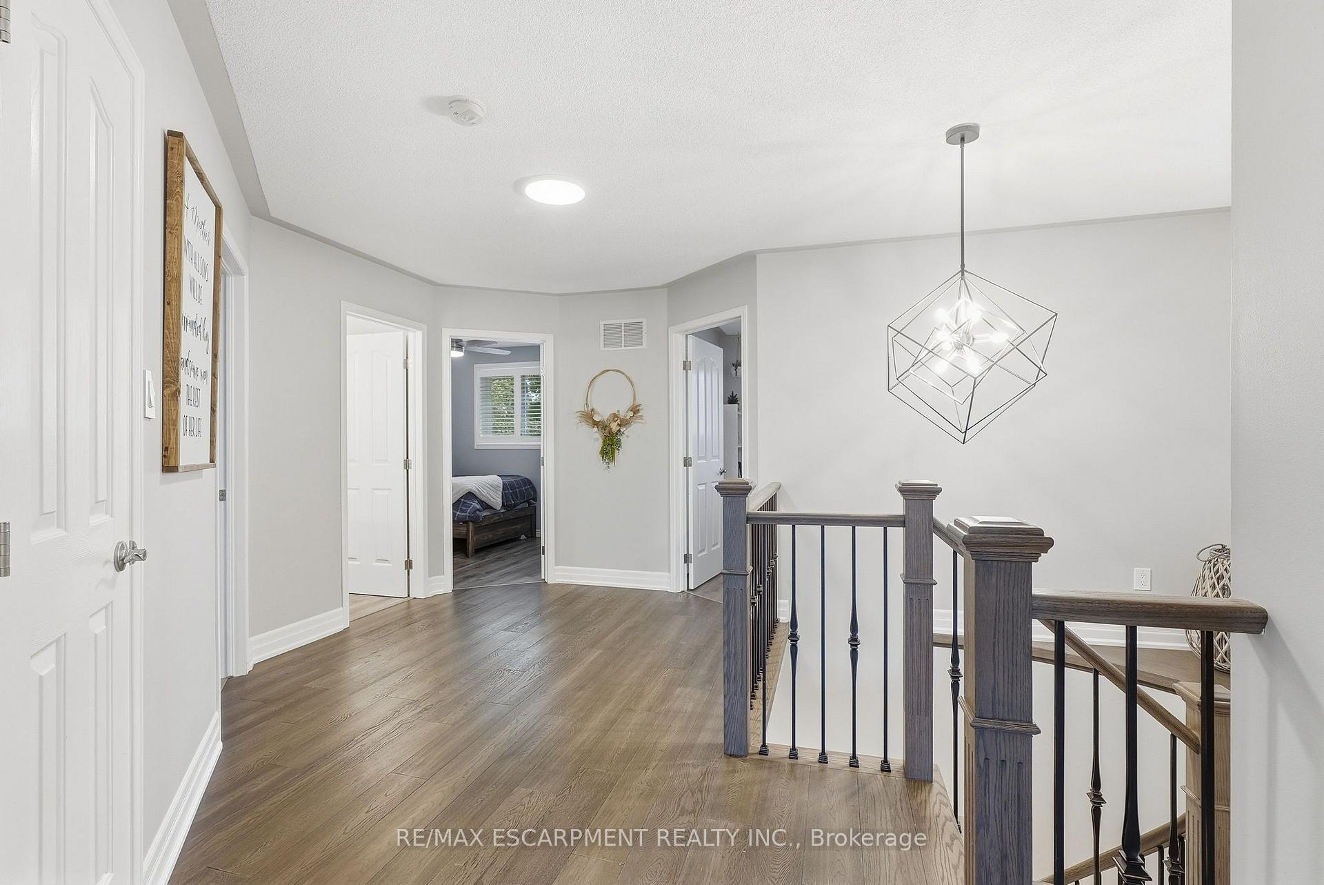 Upstairs landing with plank flooring, dark stair railings, and a geometric pendant light.