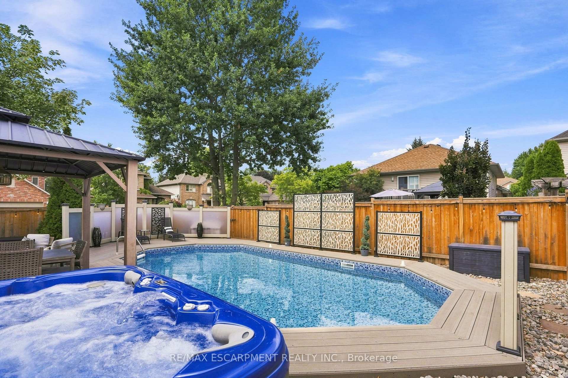 Backyard pool and bubbling hot tub beside a pergola, patio seating, and decorative privacy screens.