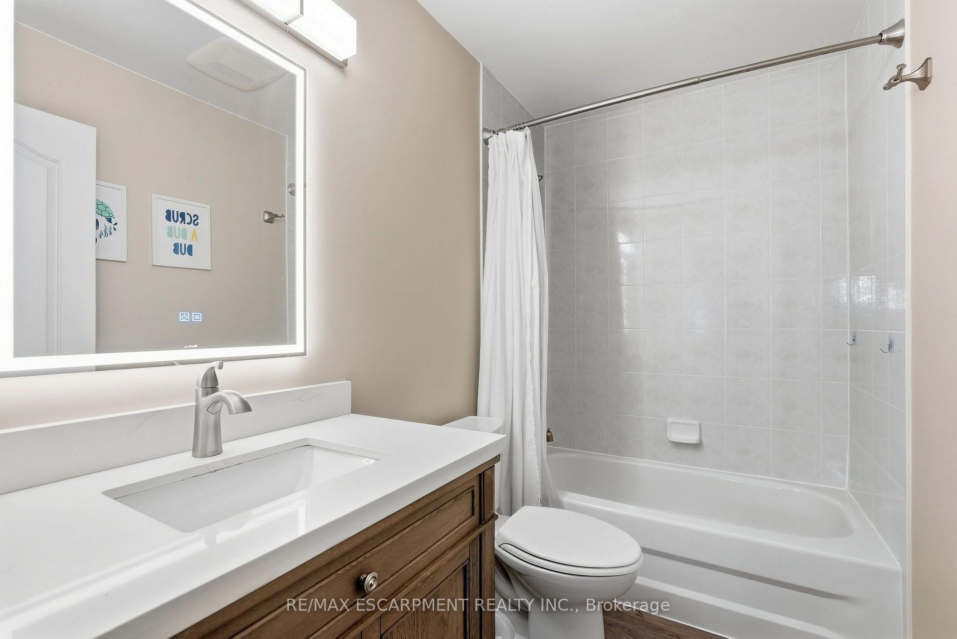 Bathroom with a tiled bathtub, white vanity, wood cabinet, and illuminated mirror.