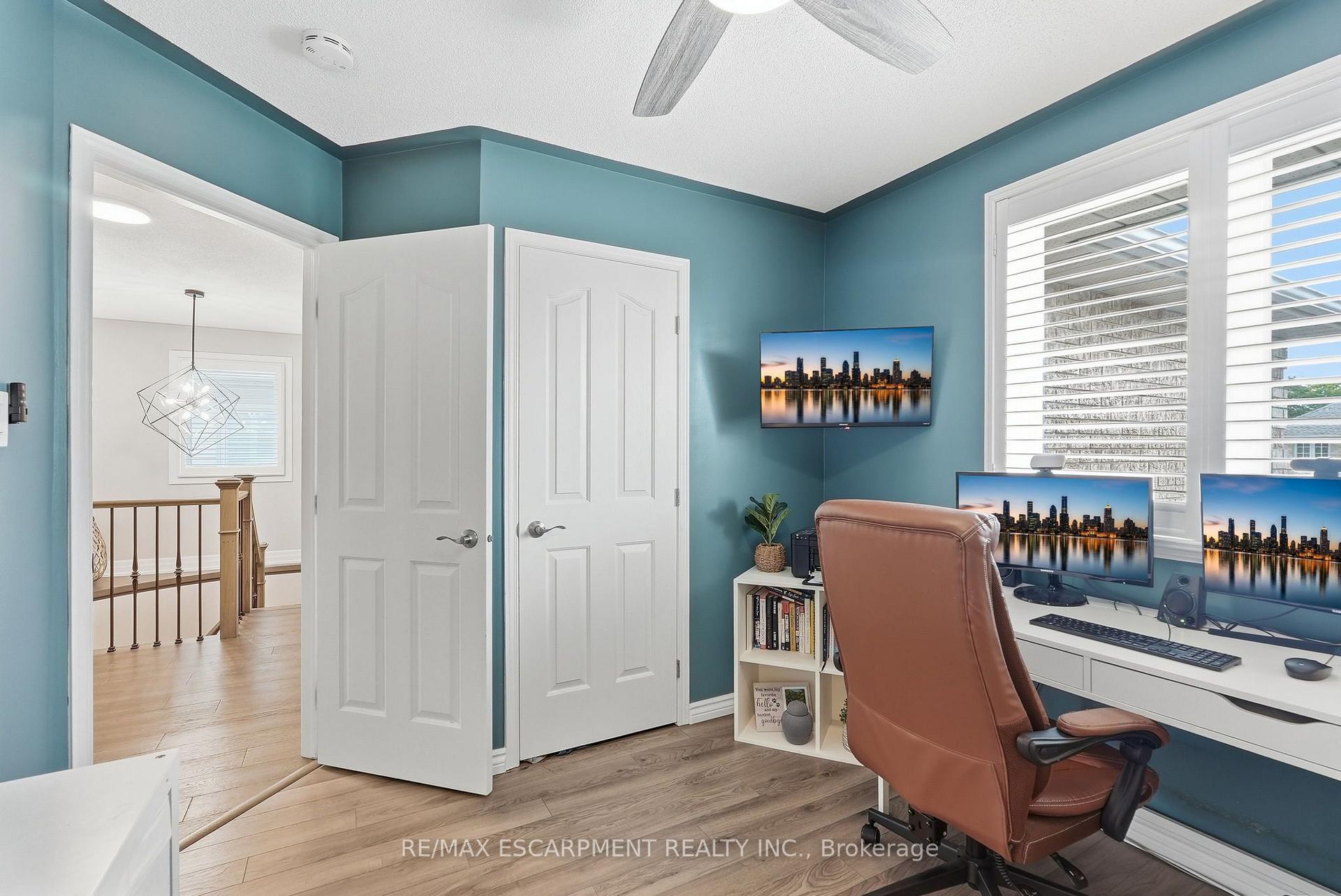 Home office with teal walls, a leather chair, and multiple monitors beside a window.