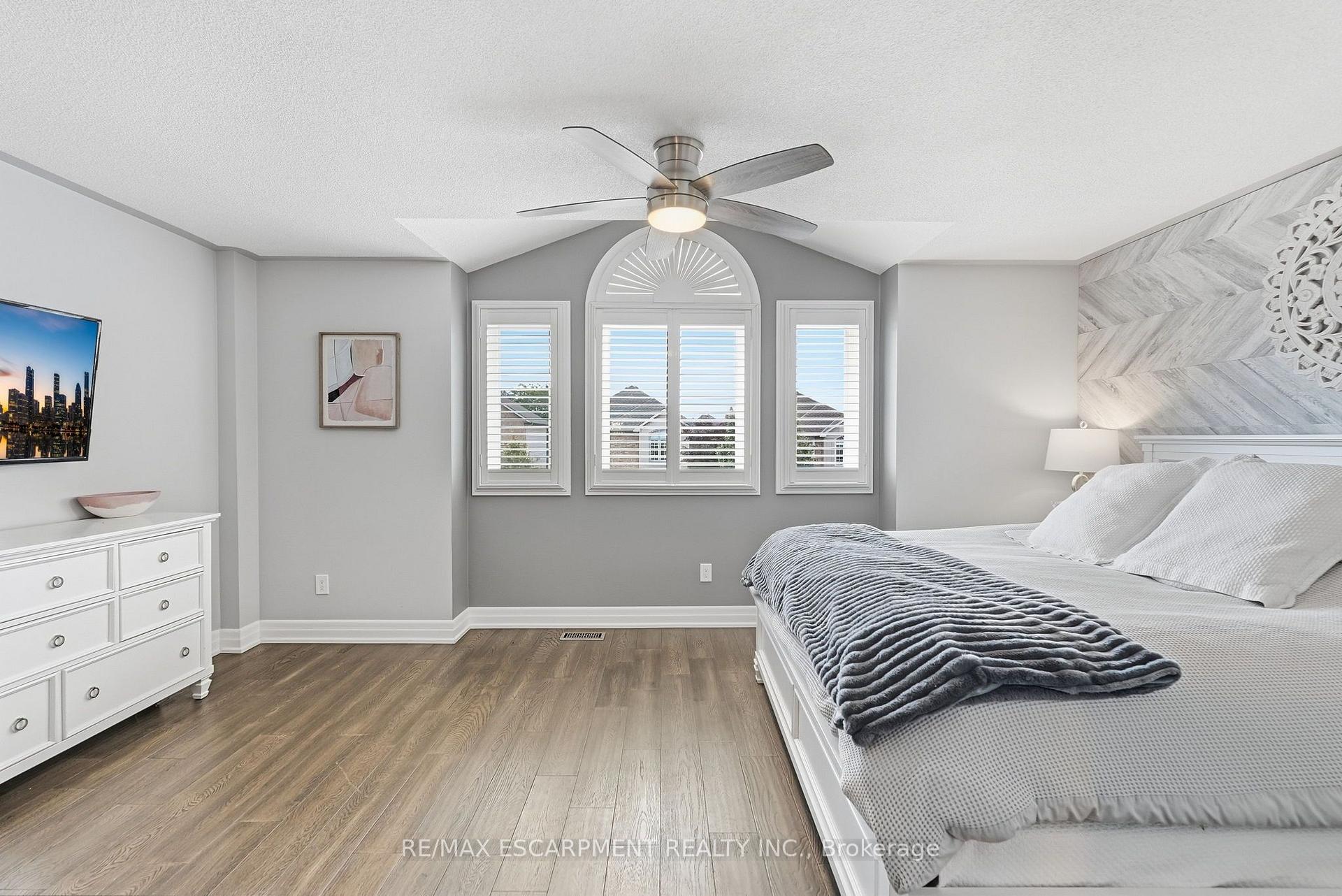 Bedroom with a white bed, wood floors, and a tall arched window with shutters.