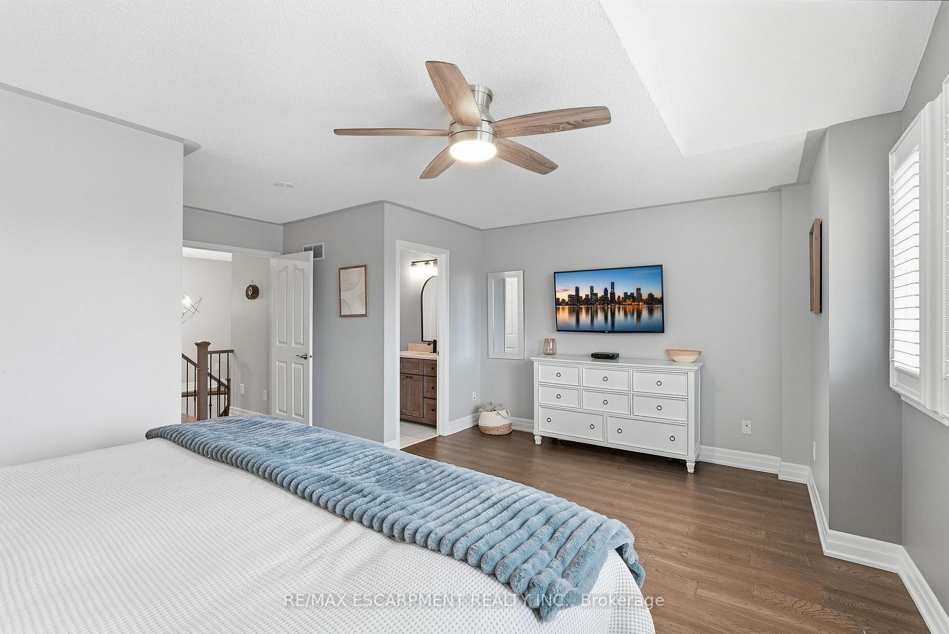 Furnished bedroom with a blue bed throw, wood-look flooring, ceiling fan, and white dresser.