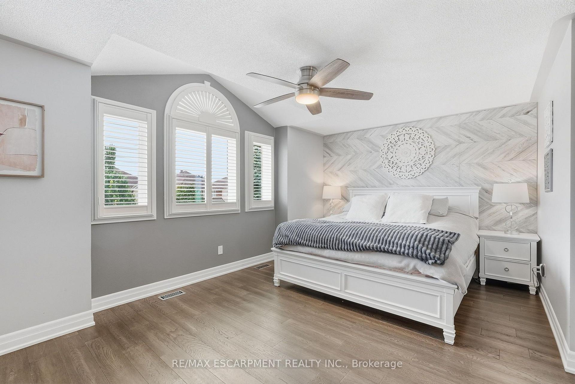 Furnished bedroom with a white bed, chevron accent wall, arched windows, and wood-look flooring.