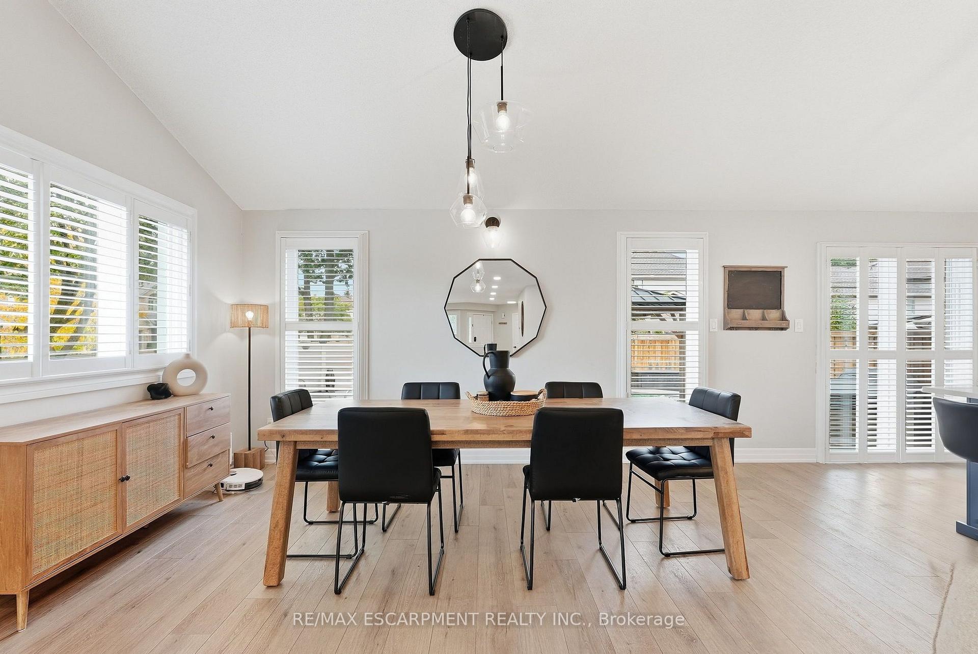 Bright dining room with a long wooden table, black chairs, shuttered windows, and glass doors.