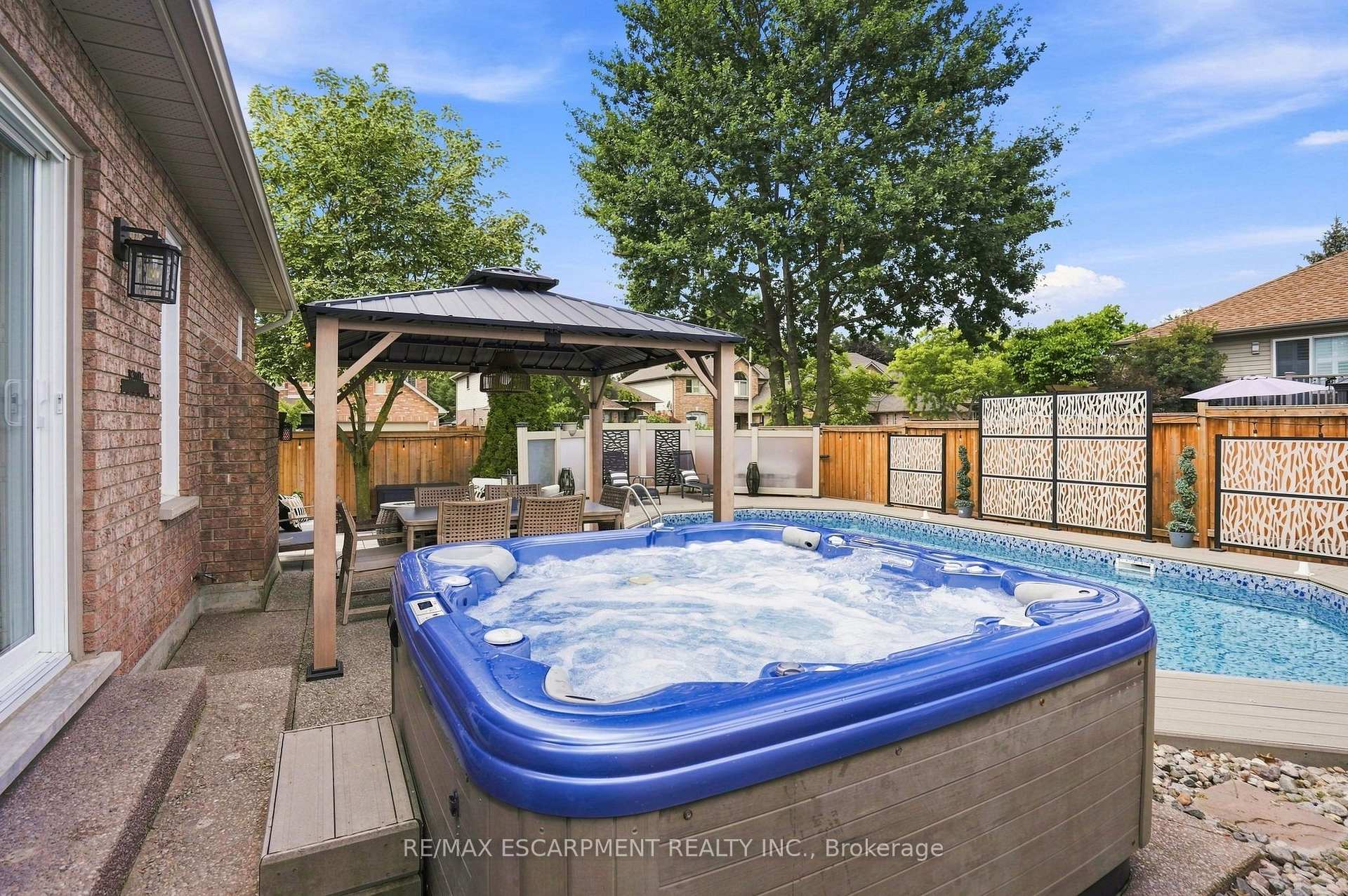 Backyard pool and blue hot tub beside a covered pergola and outdoor dining area.