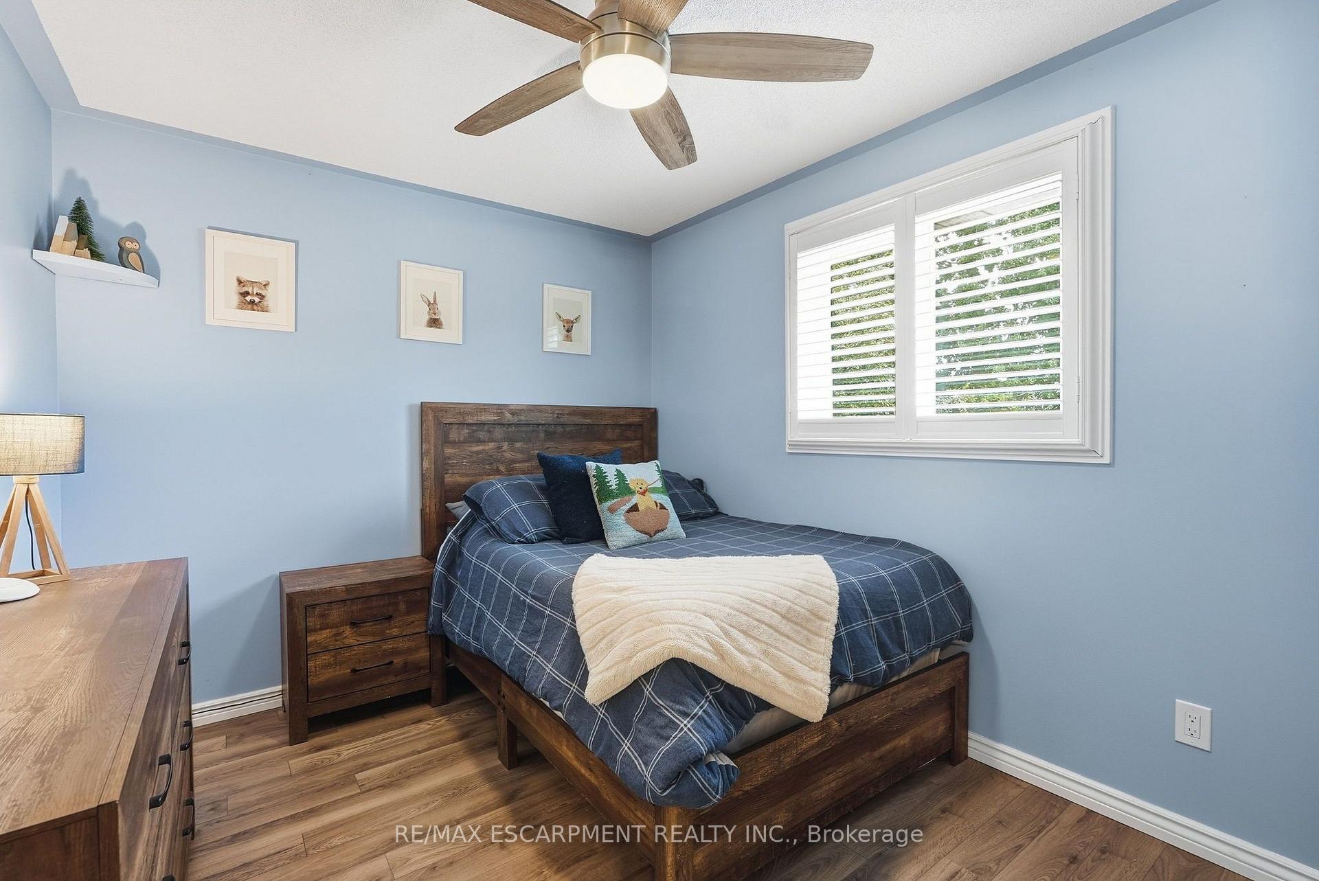 Blue bedroom with a dark wood bed, matching nightstand, and white plantation shutters.
