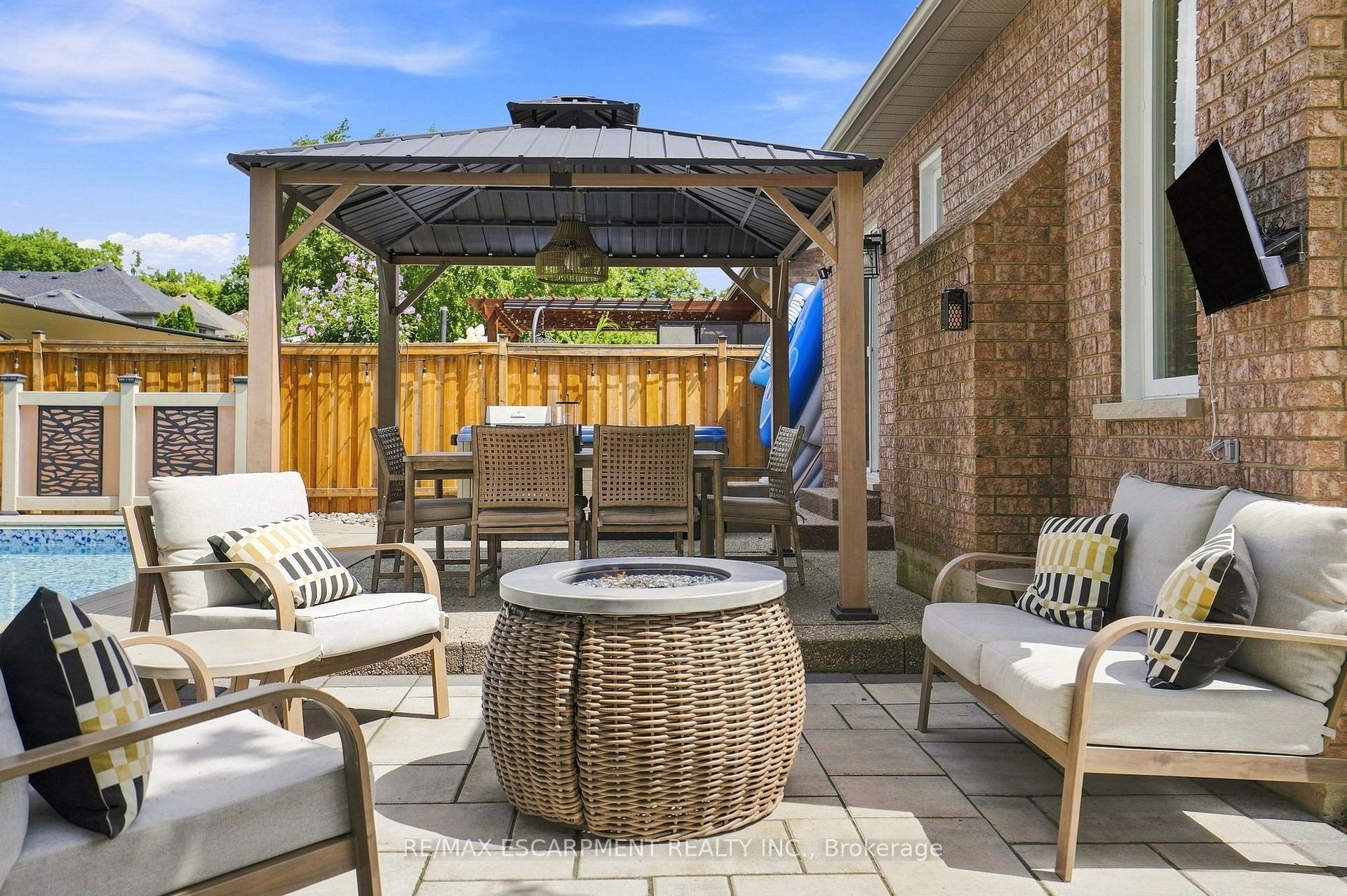 Backyard patio with a covered gazebo, outdoor dining set, fire table, cushioned seating, and a swimming pool.