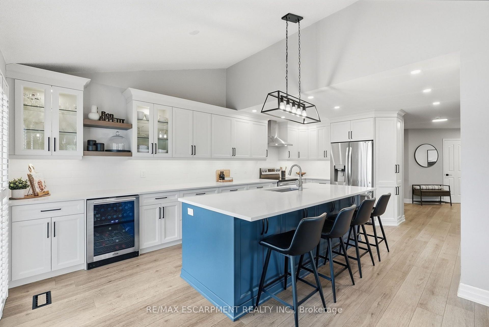 Modern kitchen with a large blue island, white cabinets, stainless steel appliances, and black bar stools.