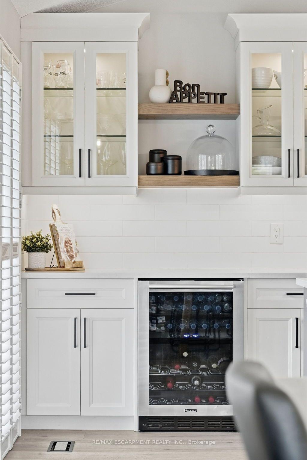 White kitchen with glass-front cabinets, wood display shelves, and a built-in wine refrigerator.