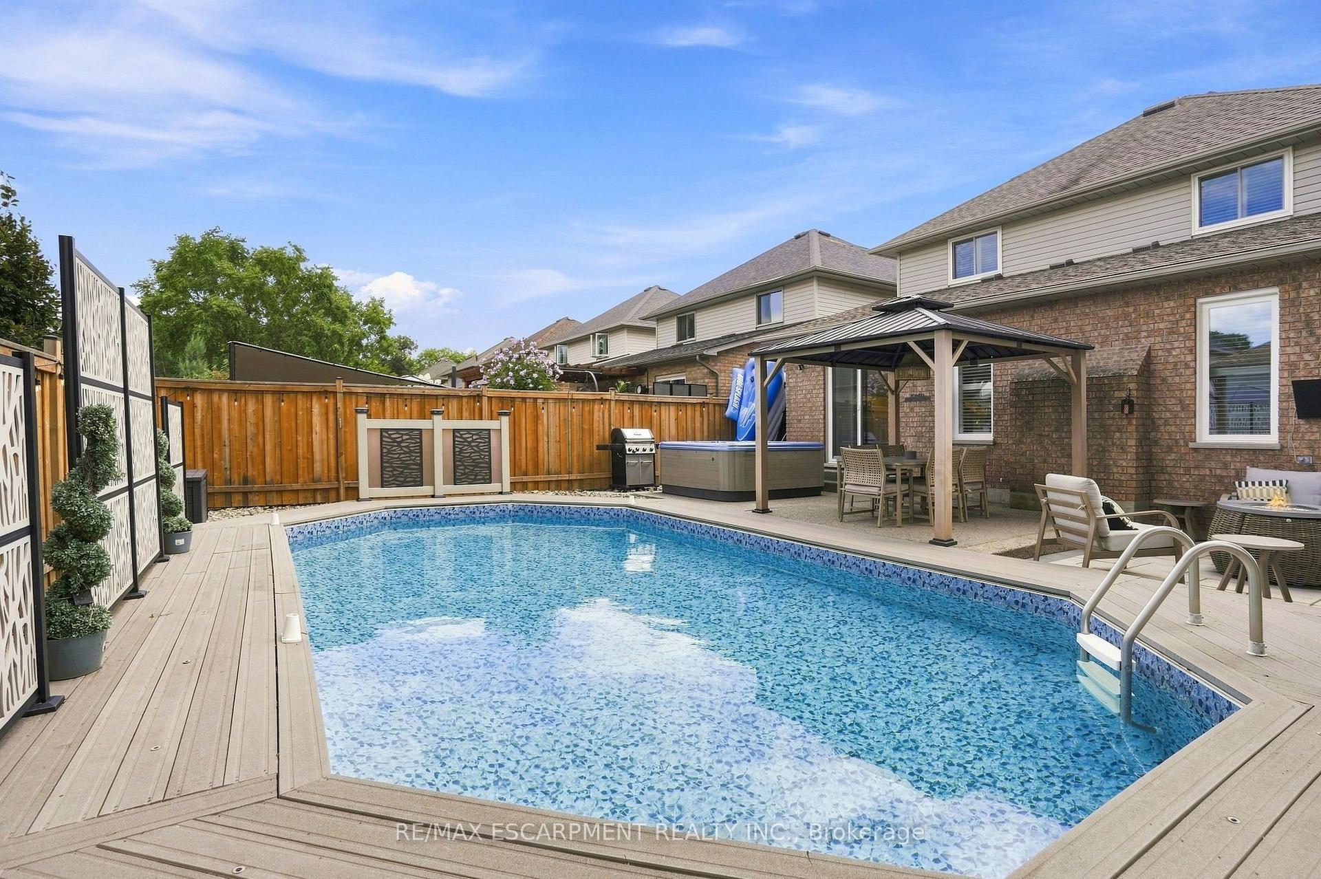 Backyard swimming pool surrounded by a deck, with a covered seating area and hot tub.