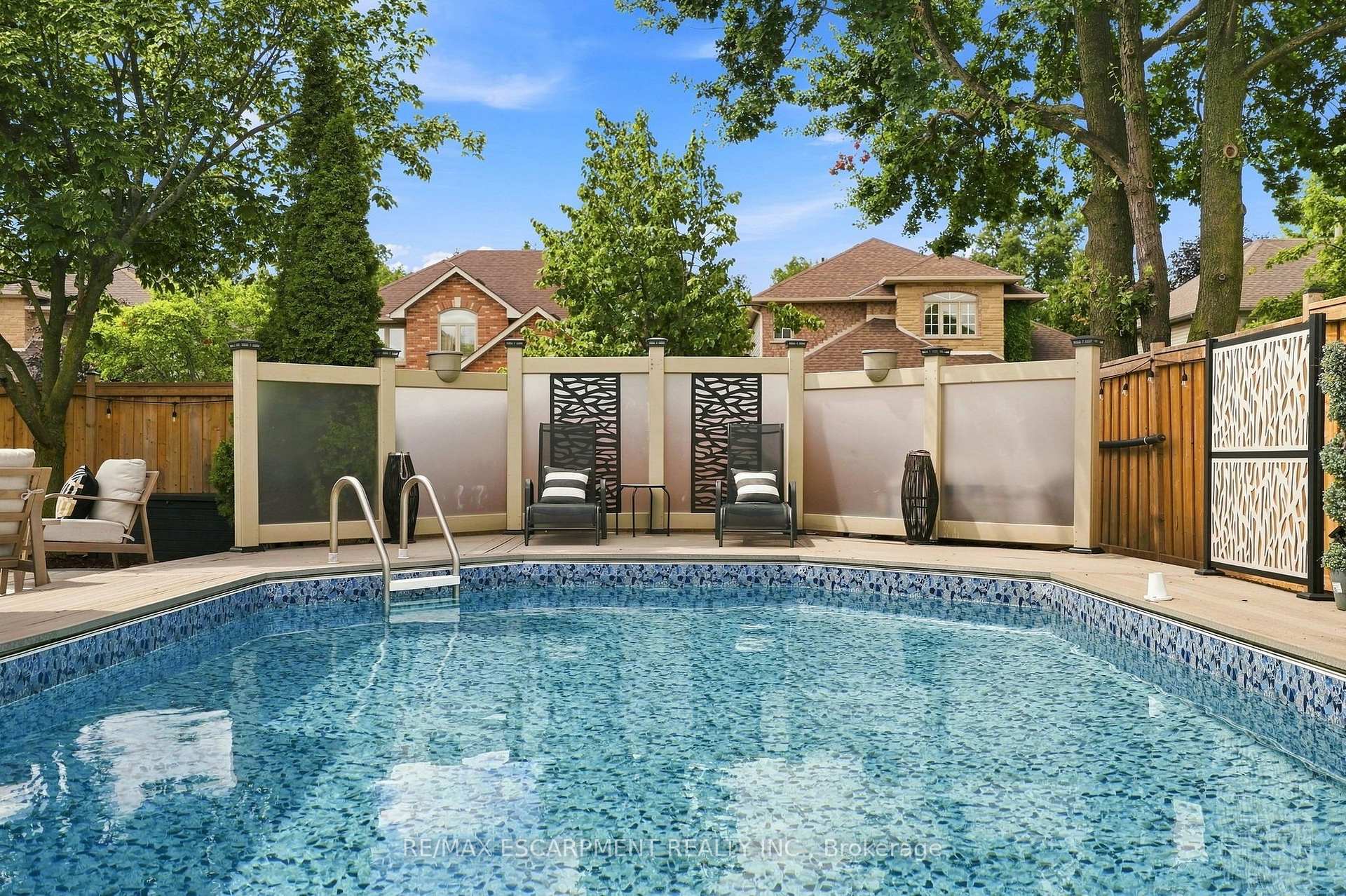 Backyard swimming pool beside a deck with lounge chairs and decorative privacy fencing.
