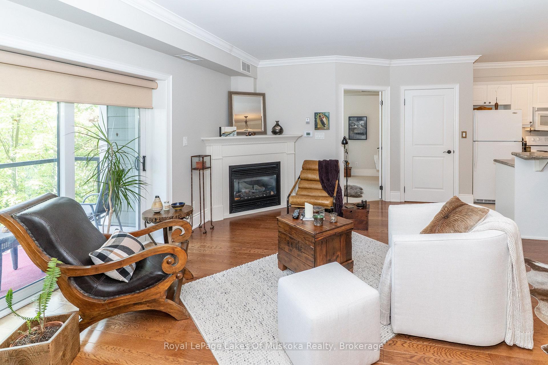 Living room with a gas fireplace, hardwood floors, and a sliding glass door overlooking leafy trees.
